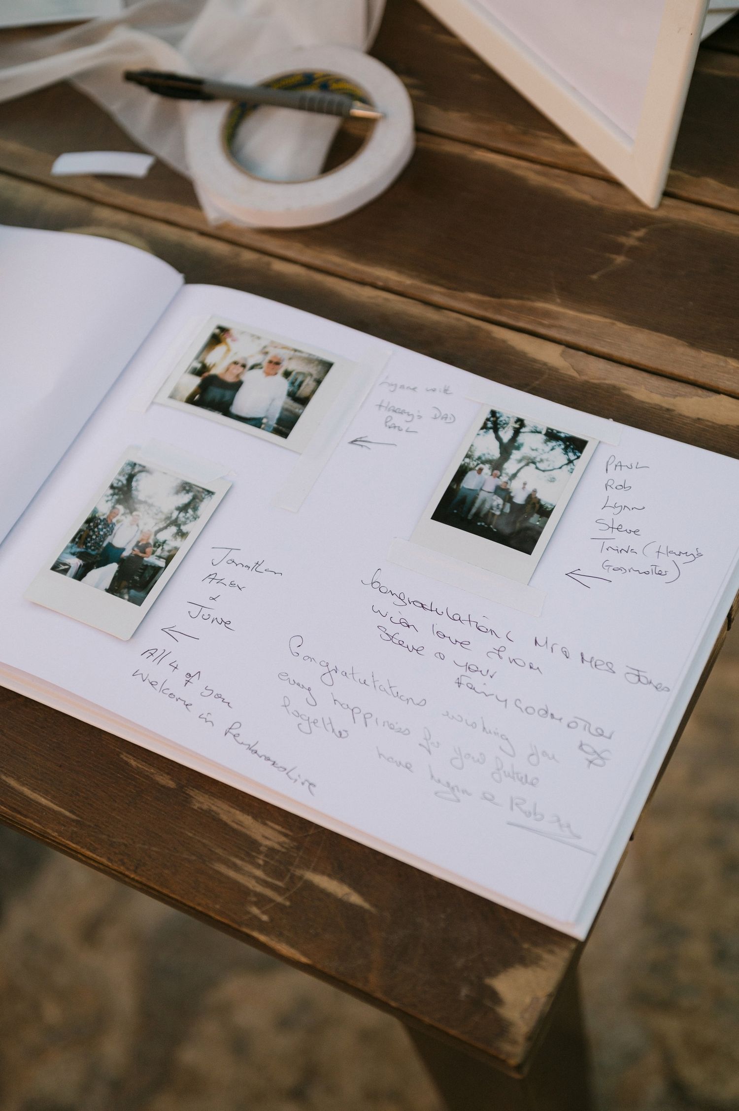A guestbook page with vintage-style polaroid photos and handwritten messages lies open on a rustic wooden surface.