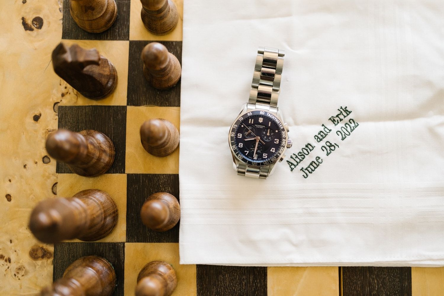 Chess pieces and a silver wristwatch arranged on a chessboard with a white napkin.