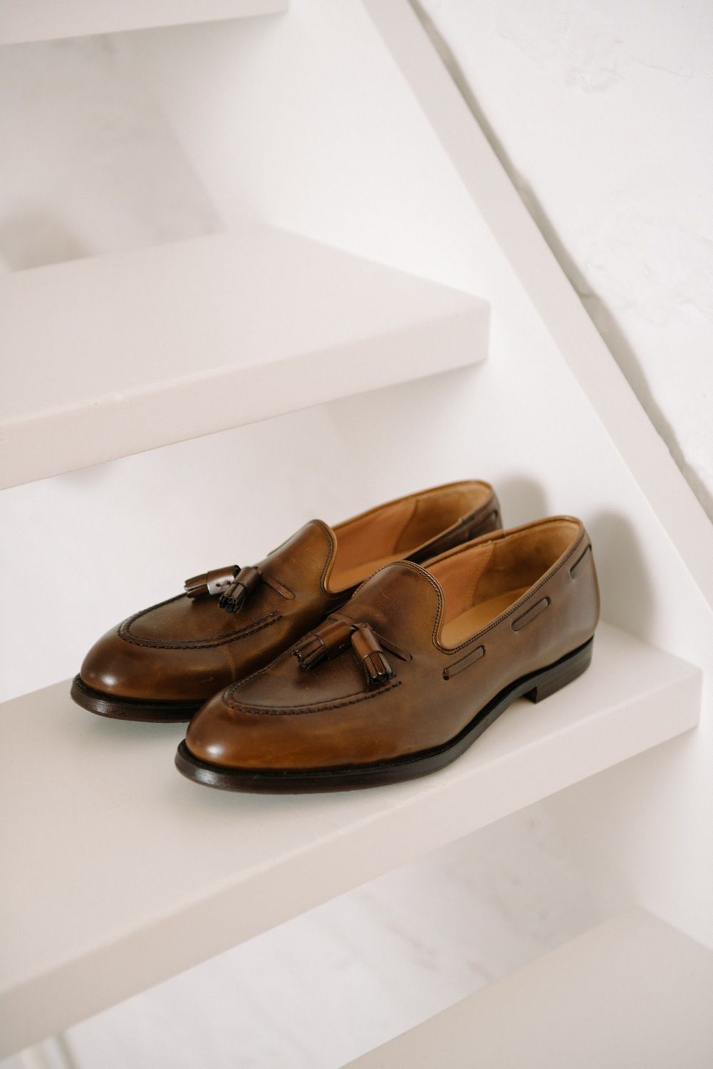 Brown leather tassel loafers on white shelves.