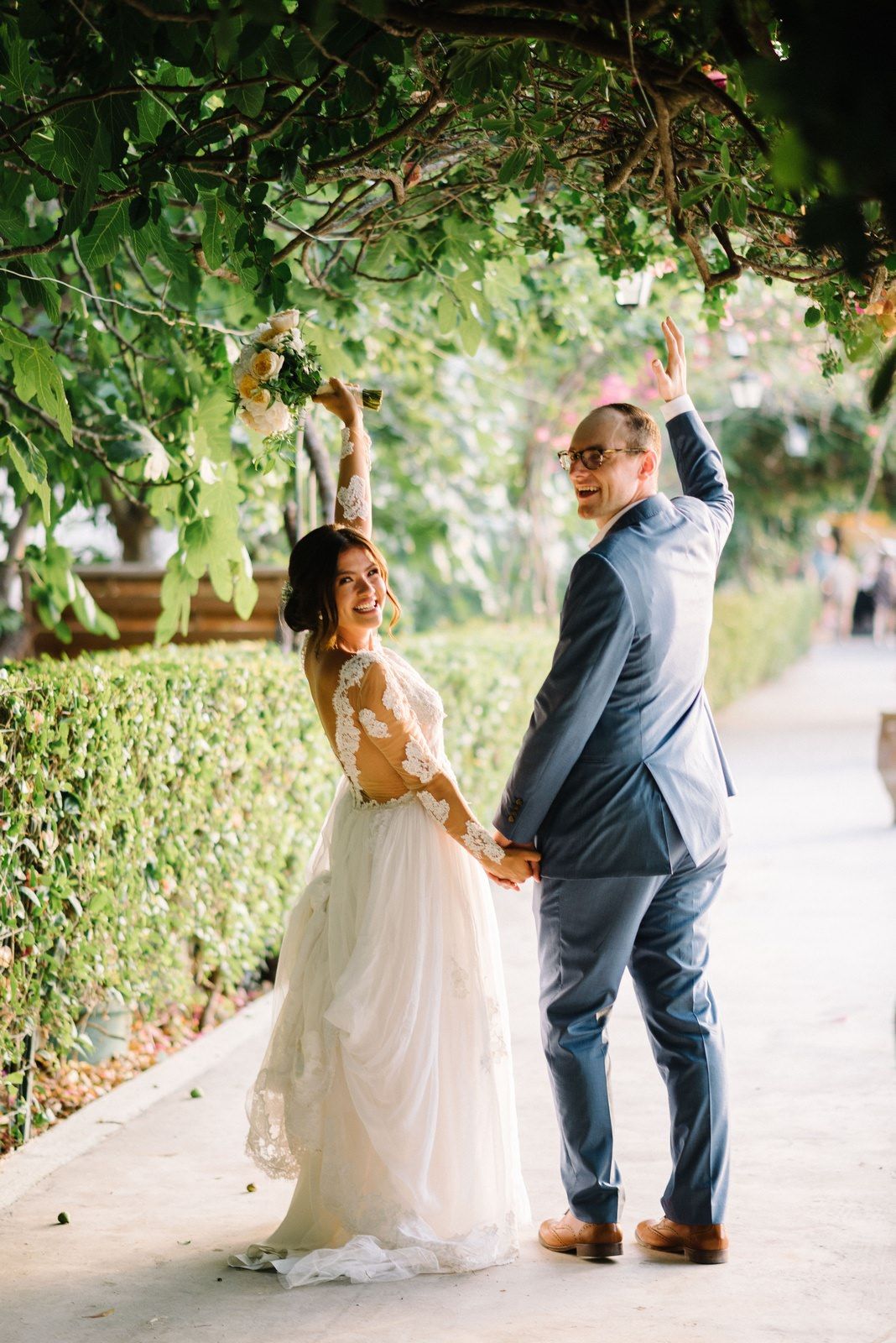 Newlyweds laughing under green vine archway in garden setting.