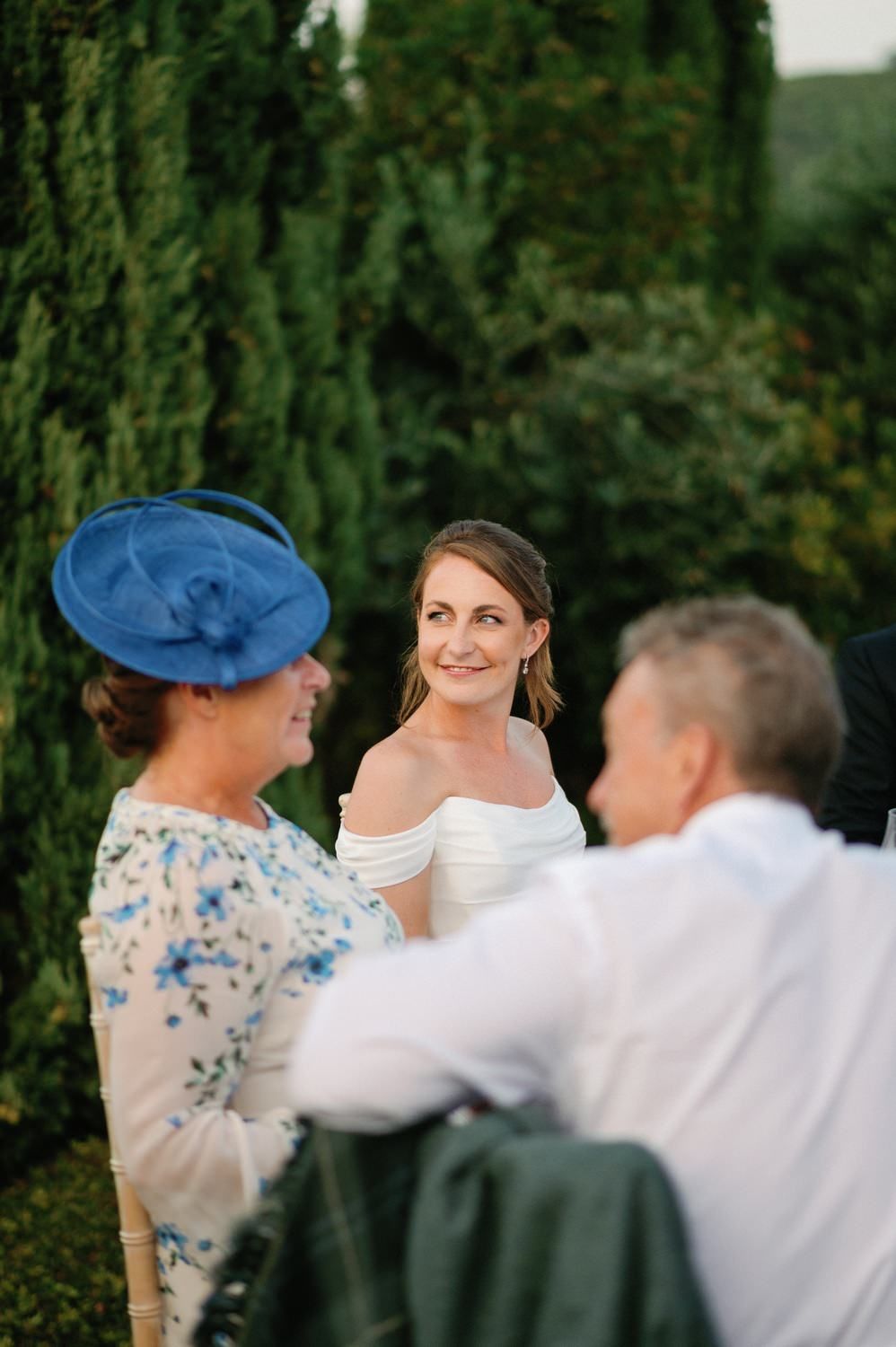 Wedding guests engage in conversation at an outdoor reception with cypress trees and coastal views.