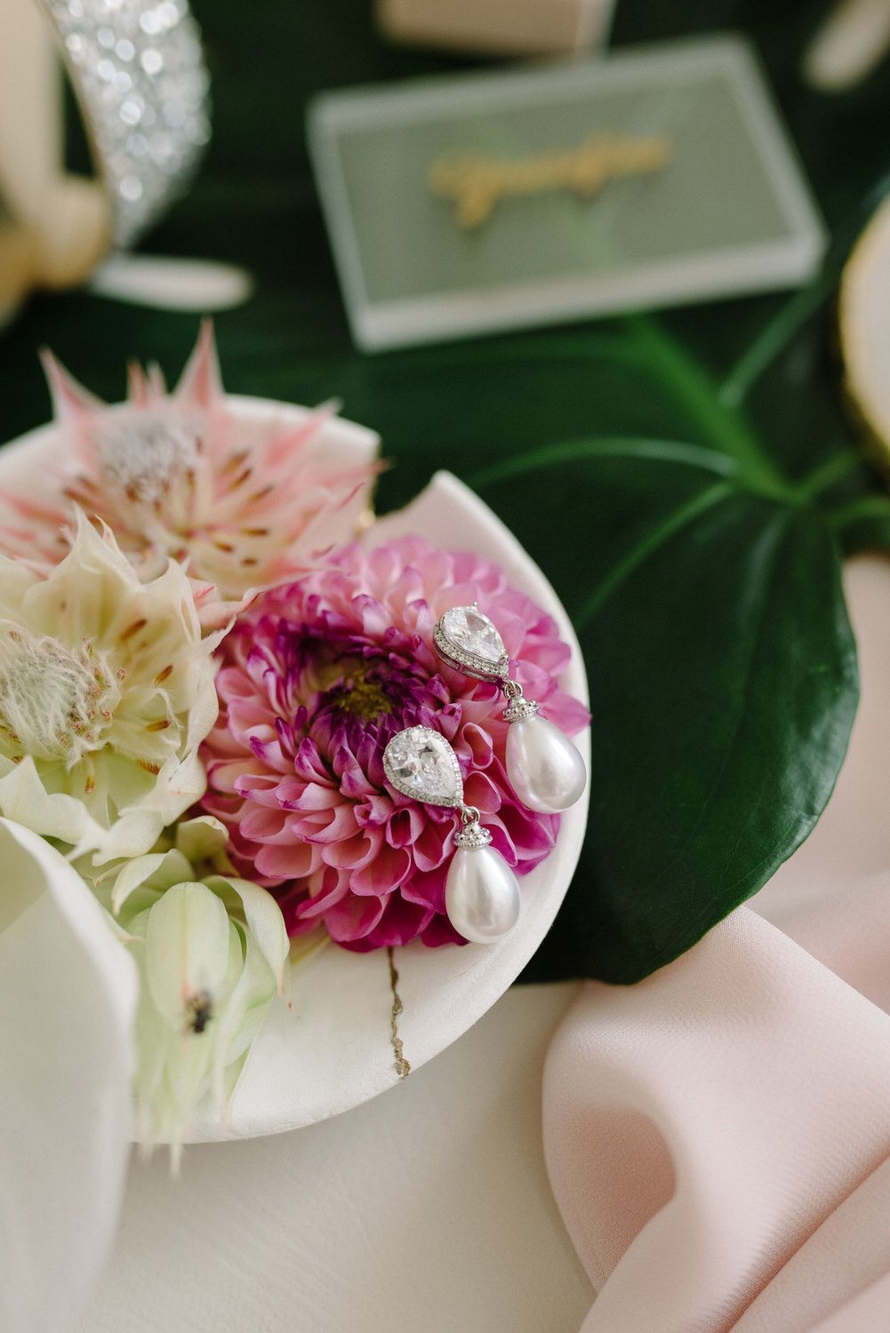 Pink and white flowers with pearls arranged on monstera leaf with soft pink fabric.