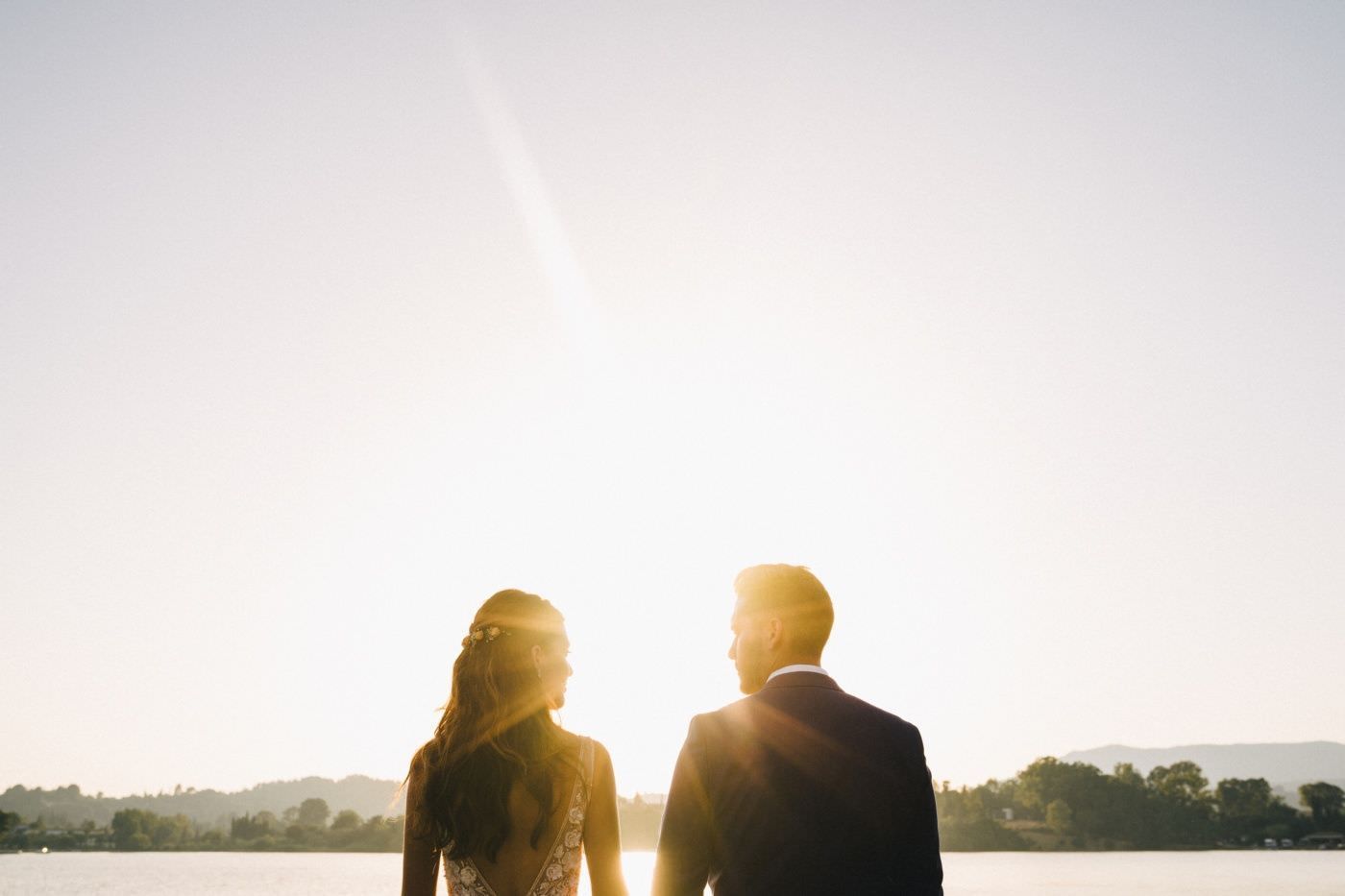 Silhouetted couple holding hands walks together during golden sunset on beach with sun rays shining through.
