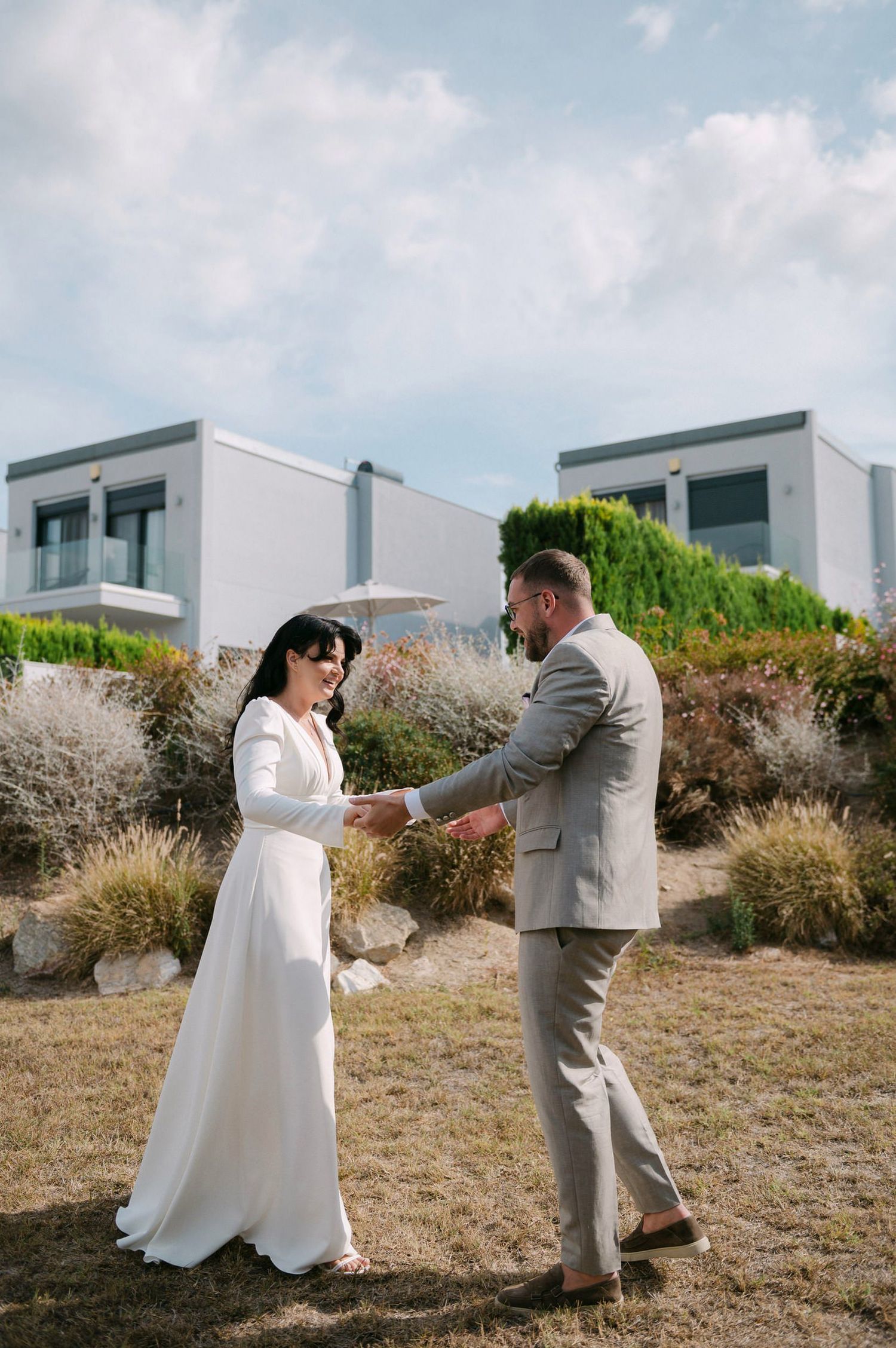 A couple dances together on a grassy hillside with modern buildings visible in the background.
