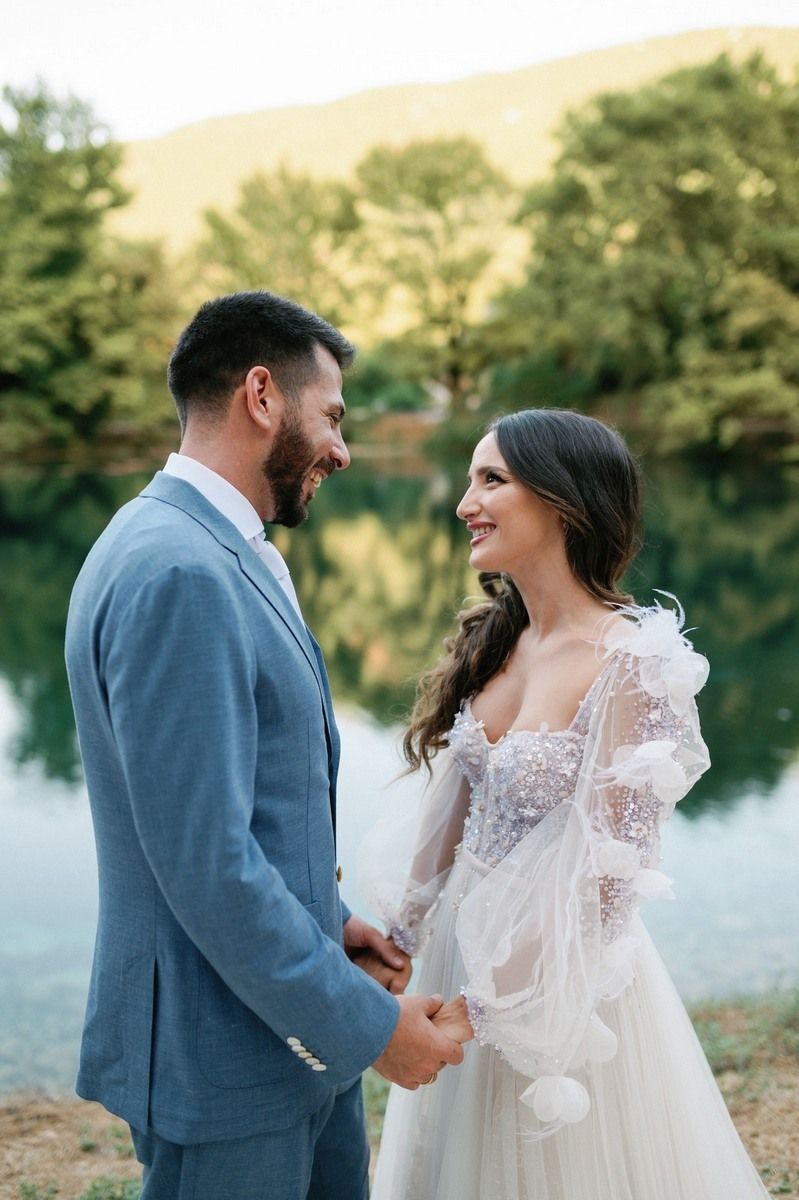 A couple shares a joyful moment by a serene lake during their outdoor wedding photoshoot.