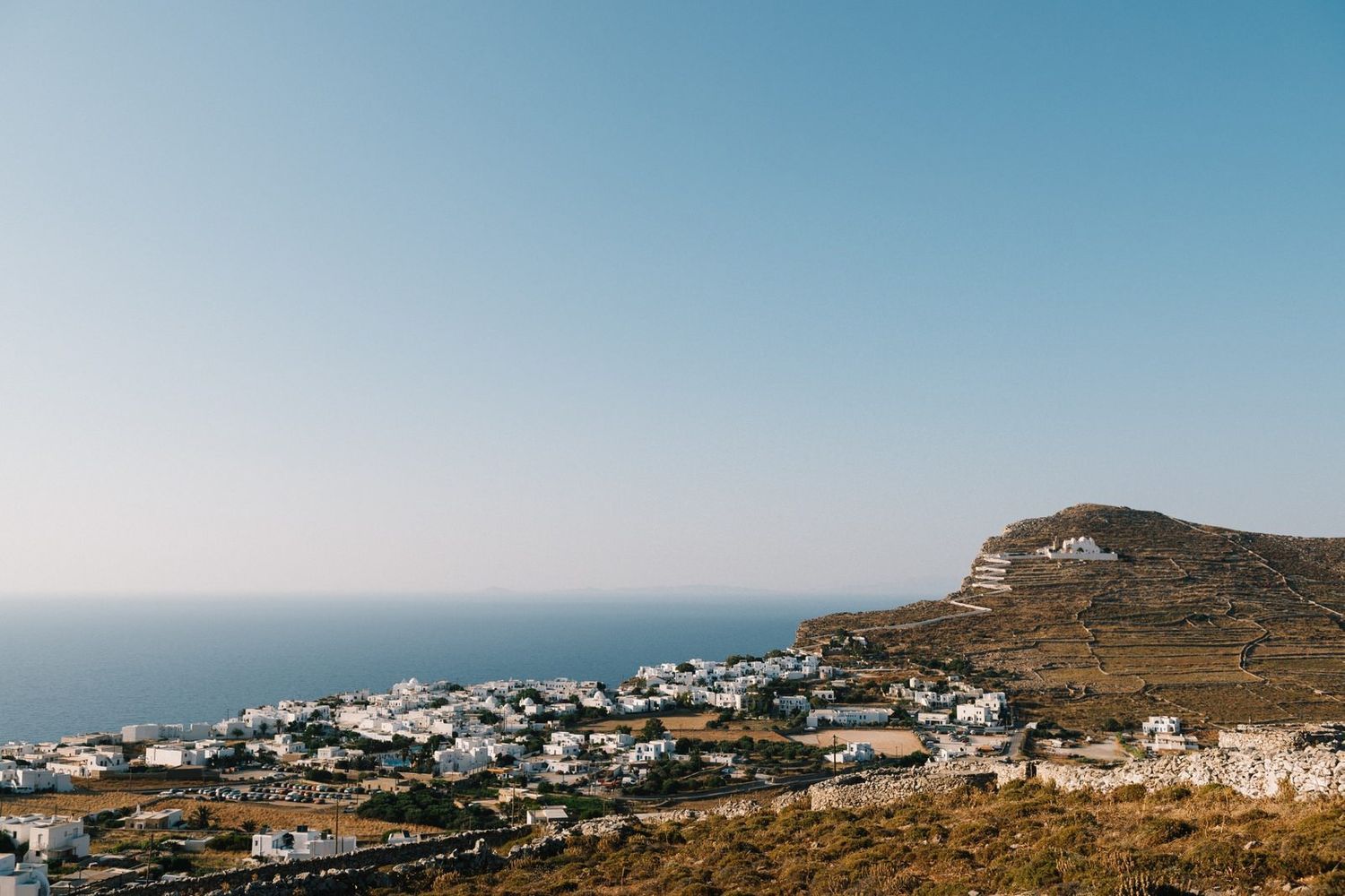Panoramic view of a coastal Mediterranean town with white buildings nestled on a hillside overlooking the sea.