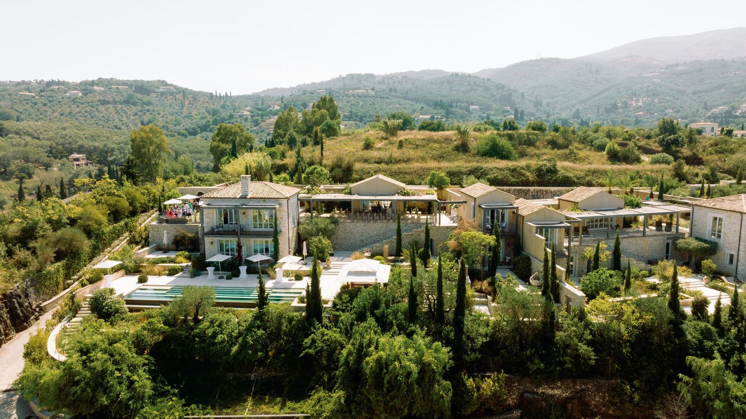 Panoramic view of rolling hills and Mediterranean landscape with scattered buildings and lush greenery.