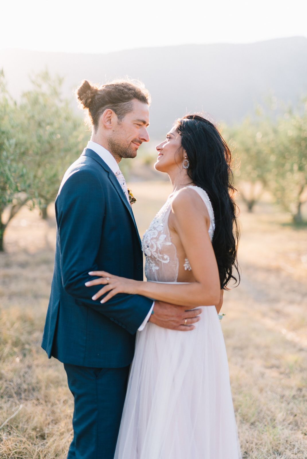 Romantic wedding couple embraces in an olive grove during golden hour sunset.
