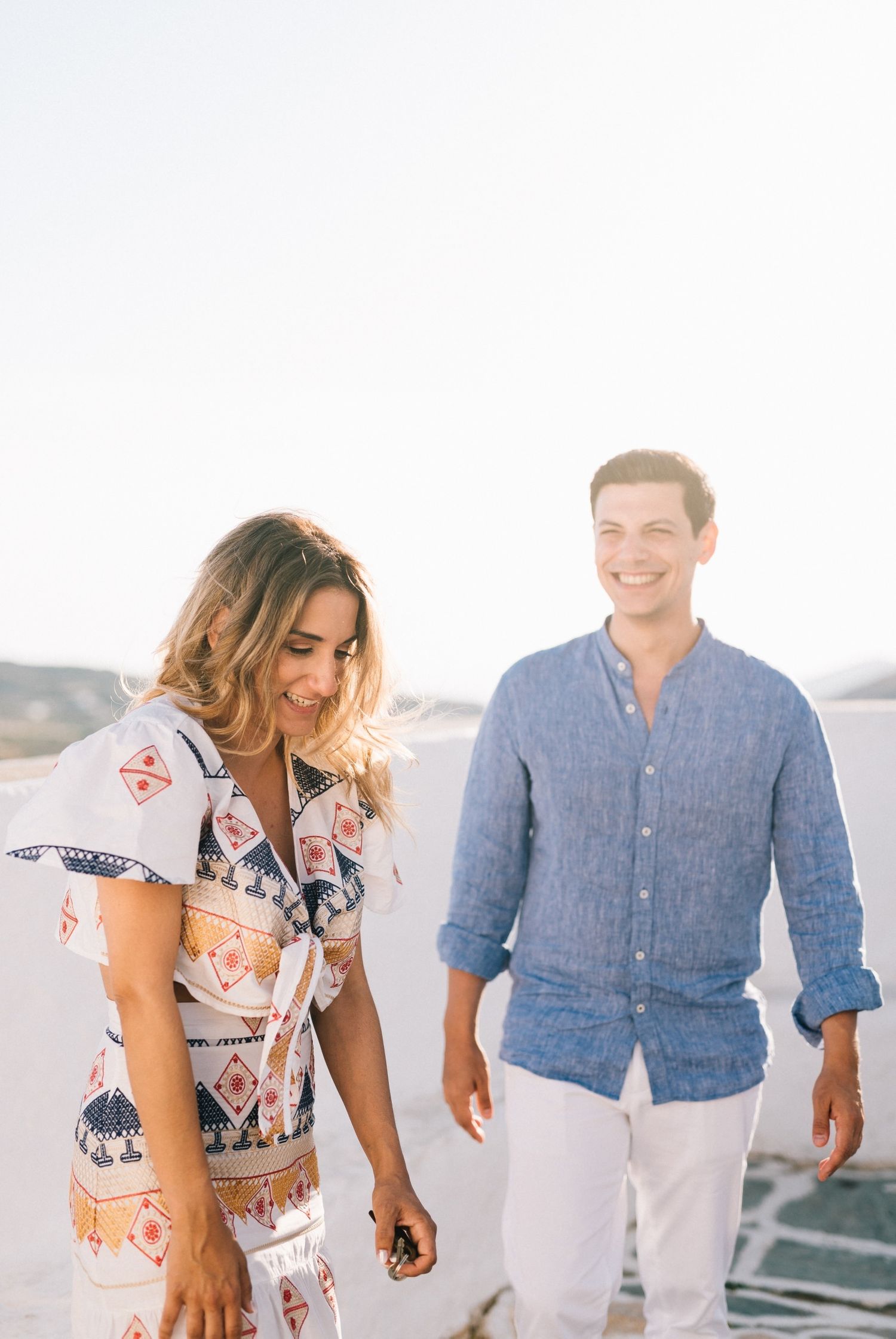 Couple in coordinated blue and white outfits walking on Mediterranean terrace.