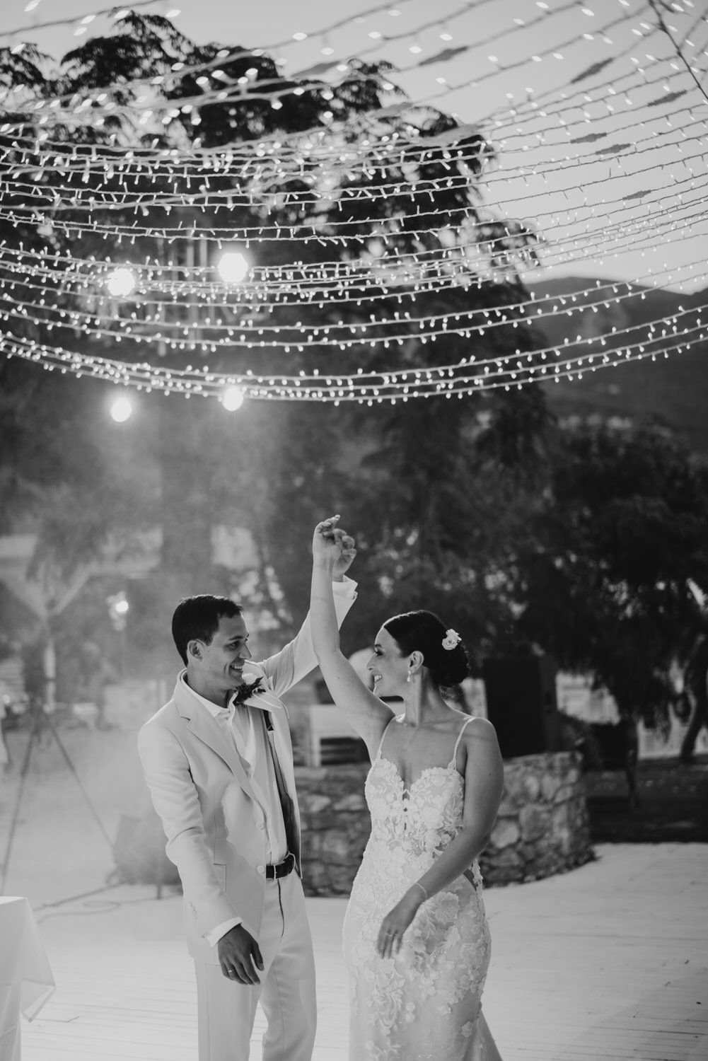 Newlyweds share a joyful dance moment under magical outdoor string light canopy.