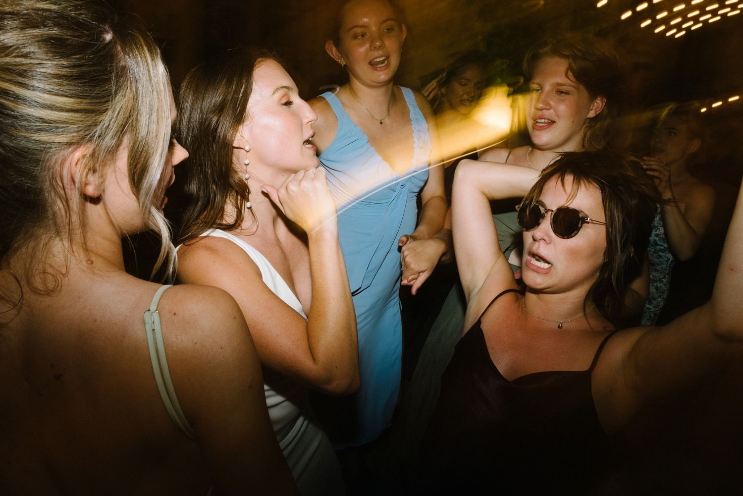 Party guests dancing and singing together in a crowded nightclub atmosphere.
