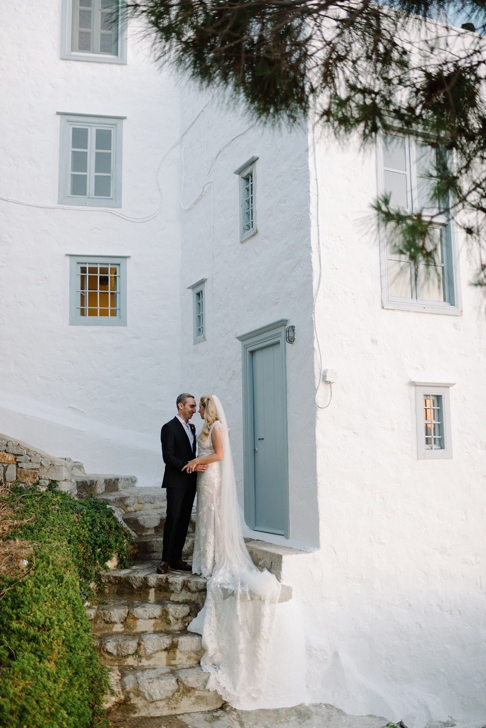 Newlyweds stand together on whitewashed stone steps of traditional Mediterranean building.
