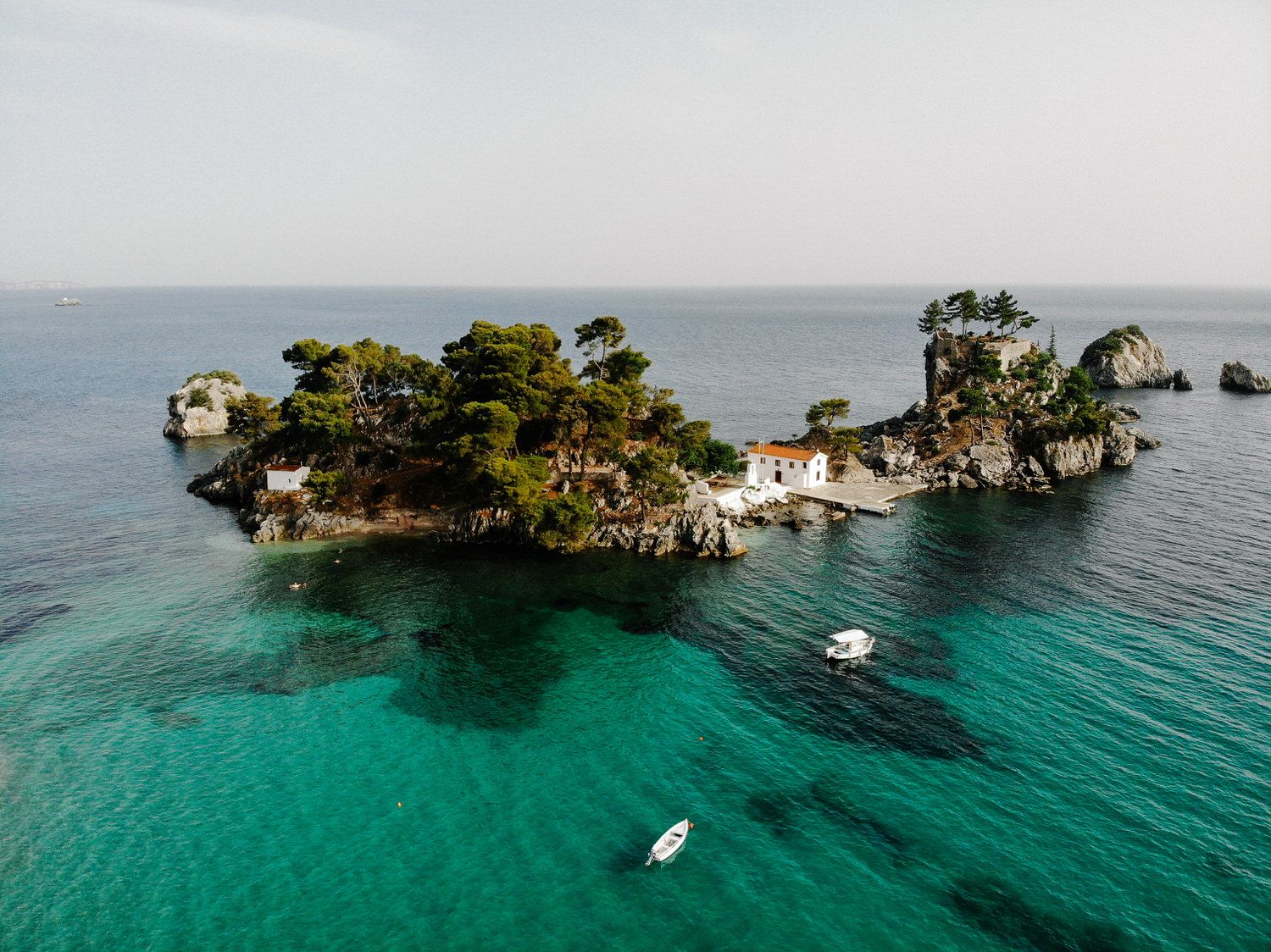 An aerial view of a tropical island with turquoise waters and boats anchored near its rocky shore.