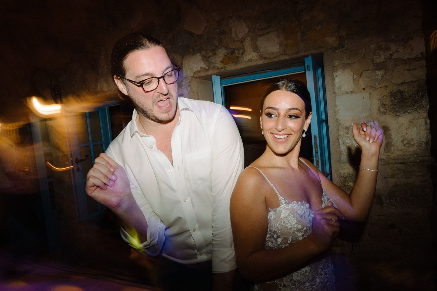 Couple dances together at wedding celebration with atmospheric lighting and stone walls.