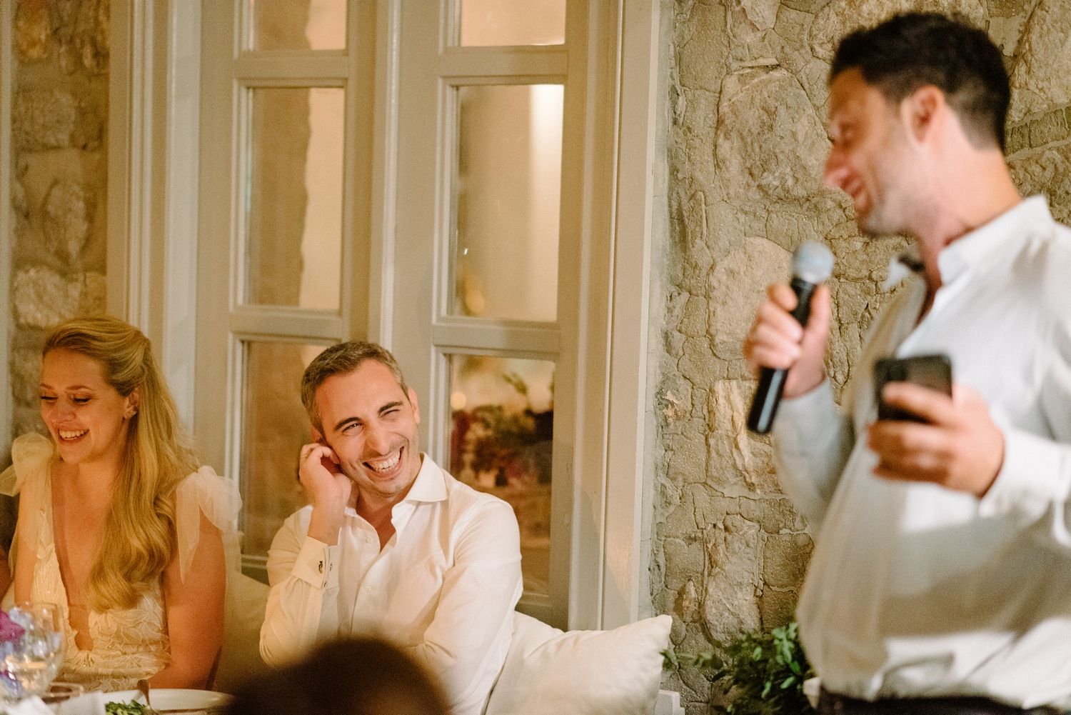 Wedding reception toasts and speeches with stone walls and window panes in background.