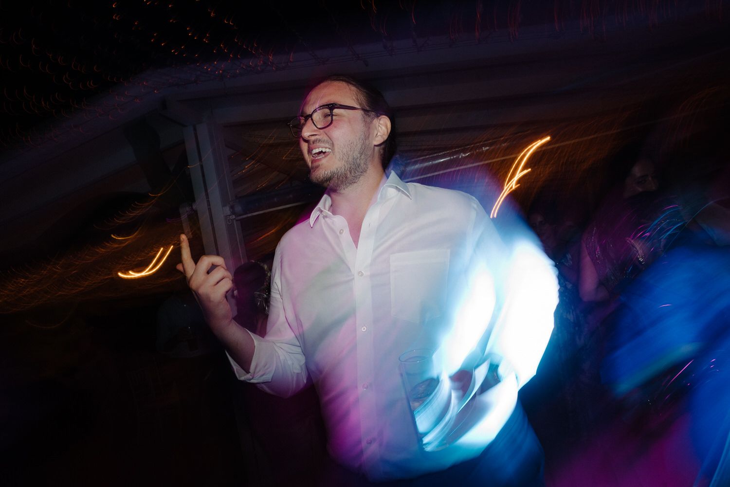 Dynamic nightclub lighting illuminates dancing guests at wedding reception.