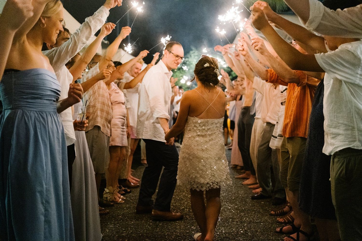Wedding guests form an archway tunnel for the newlyweds' grand exit under twinkling nighttime lights.