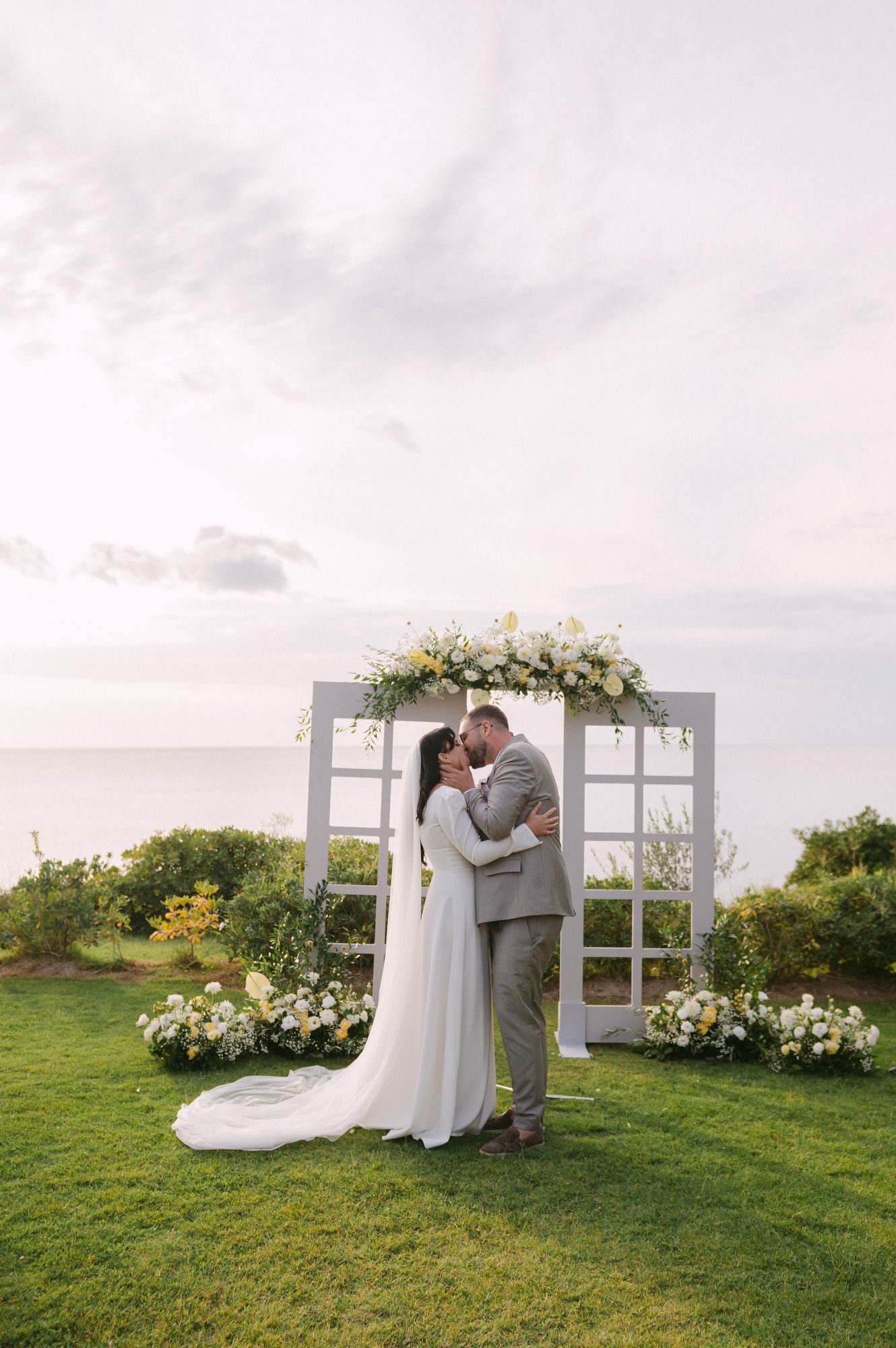 An intimate wedding moment captured against a decorative window-frame backdrop, with floral arrangements in Halkidiki Greece.