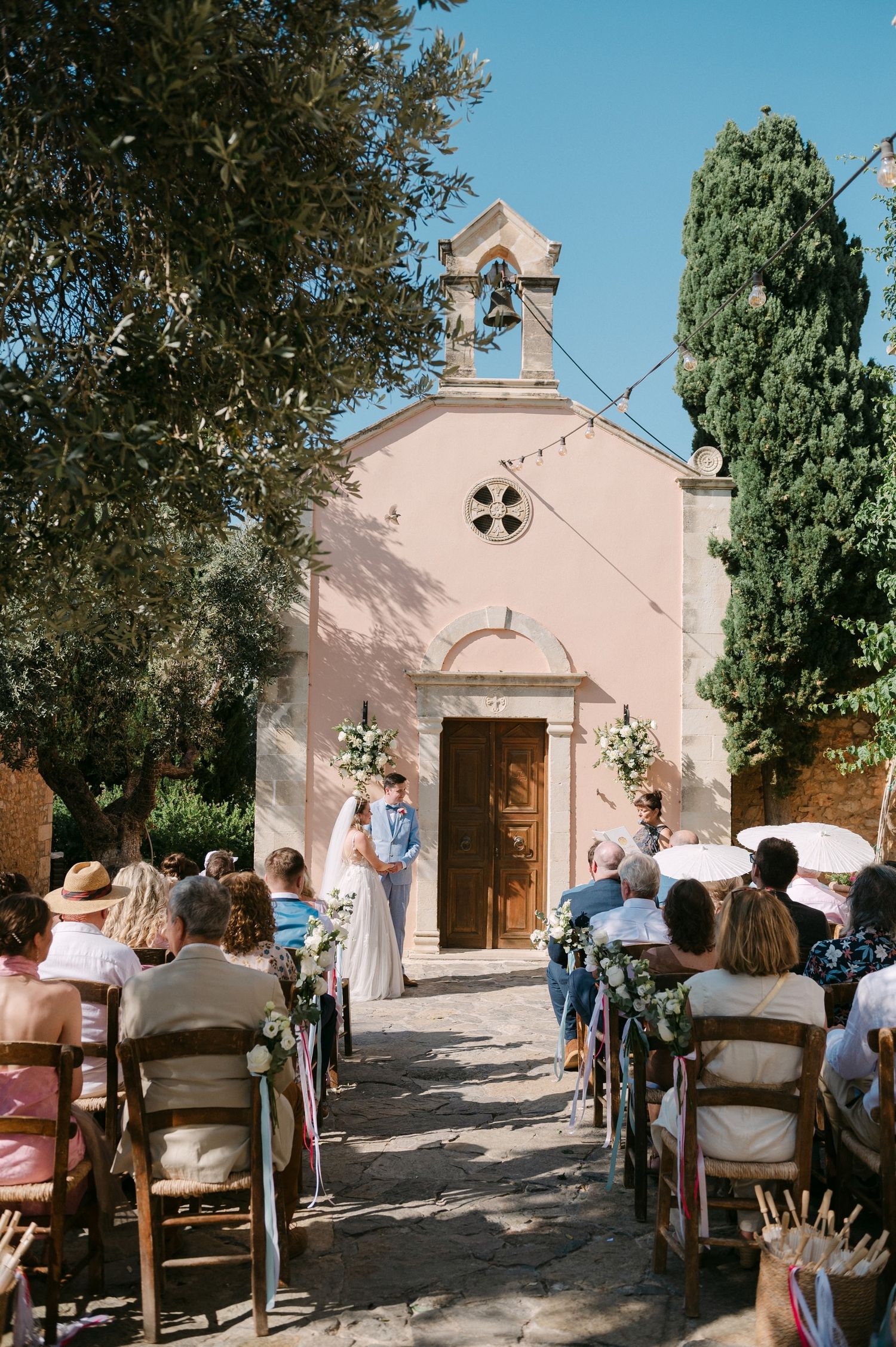 A sequence of outdoor church ceremony photos showing guests seated on wooden chairs facing a small pink chapel.