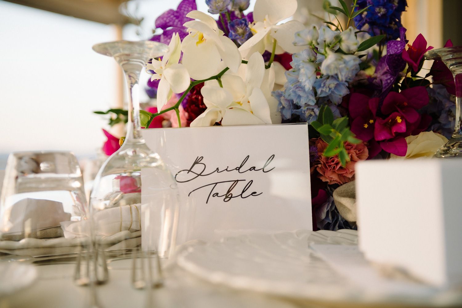 Elegant wedding table setting with handwritten place card, wine glass and colorful floral centerpiece.