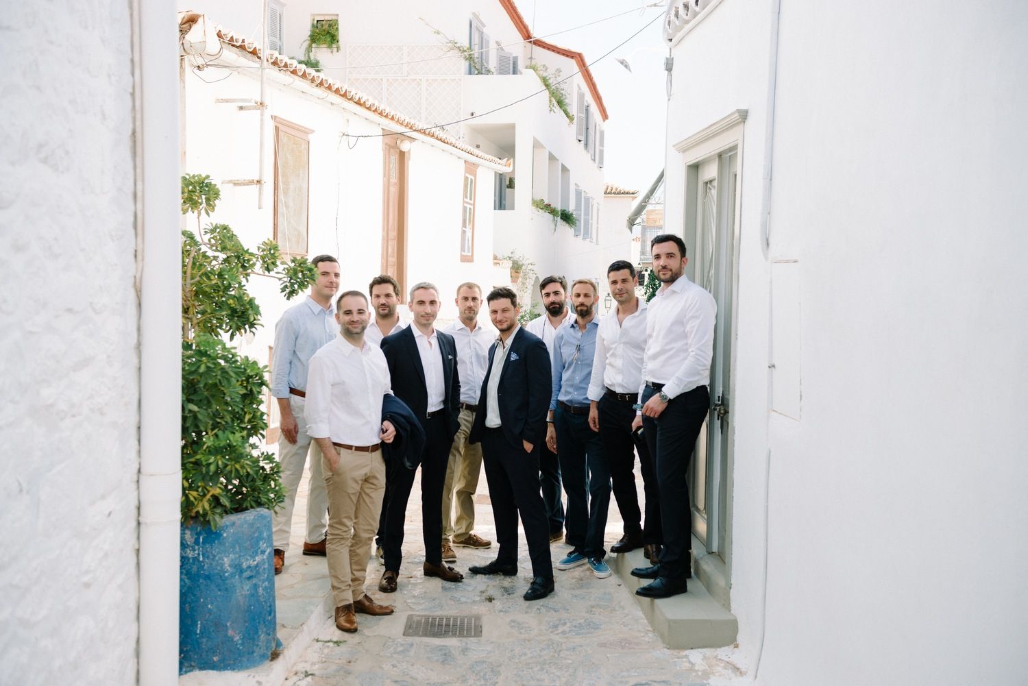 A group of formally dressed people gathered in a narrow Mediterranean alleyway.