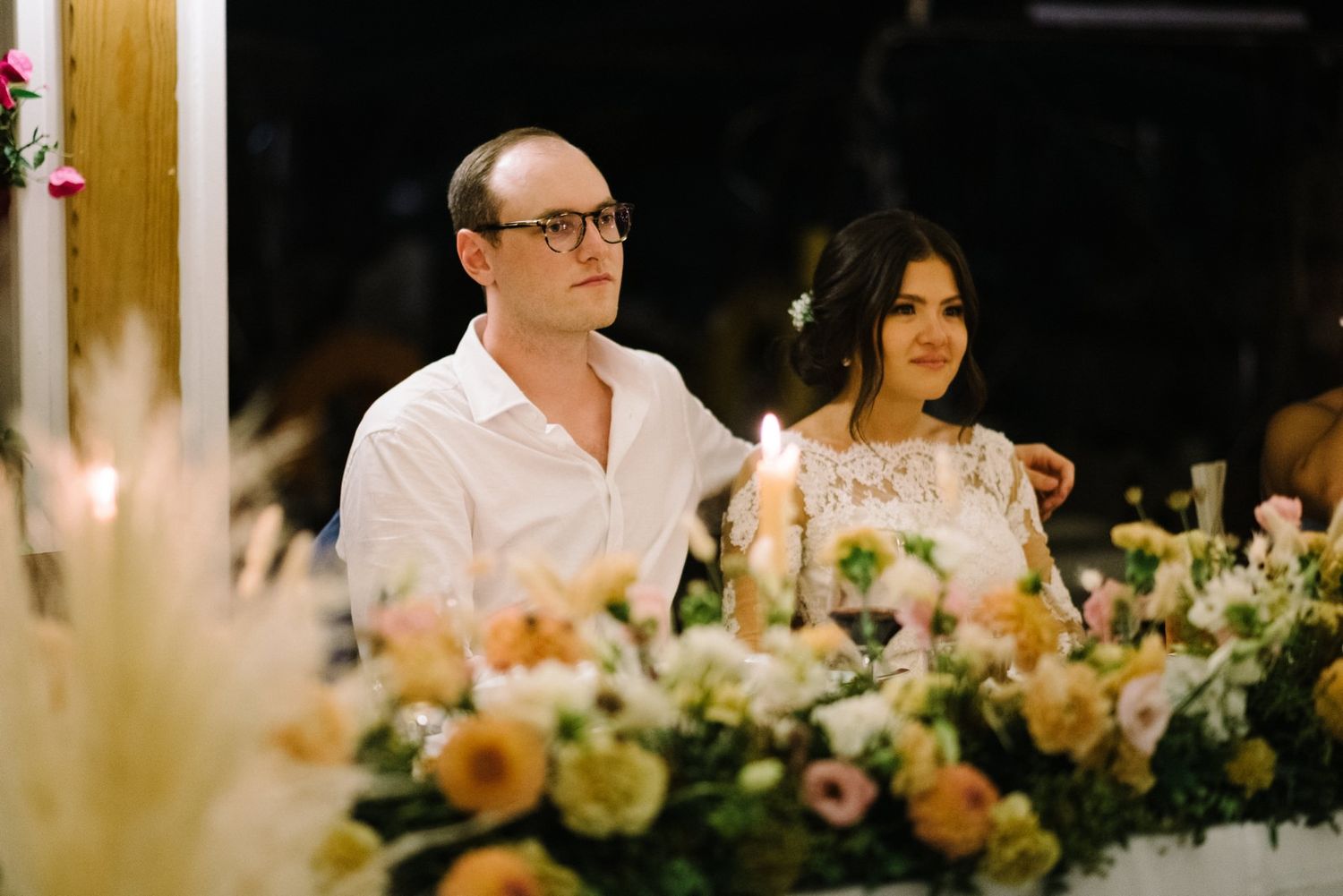 Wedding couple seated at reception table with elegant floral decorations.