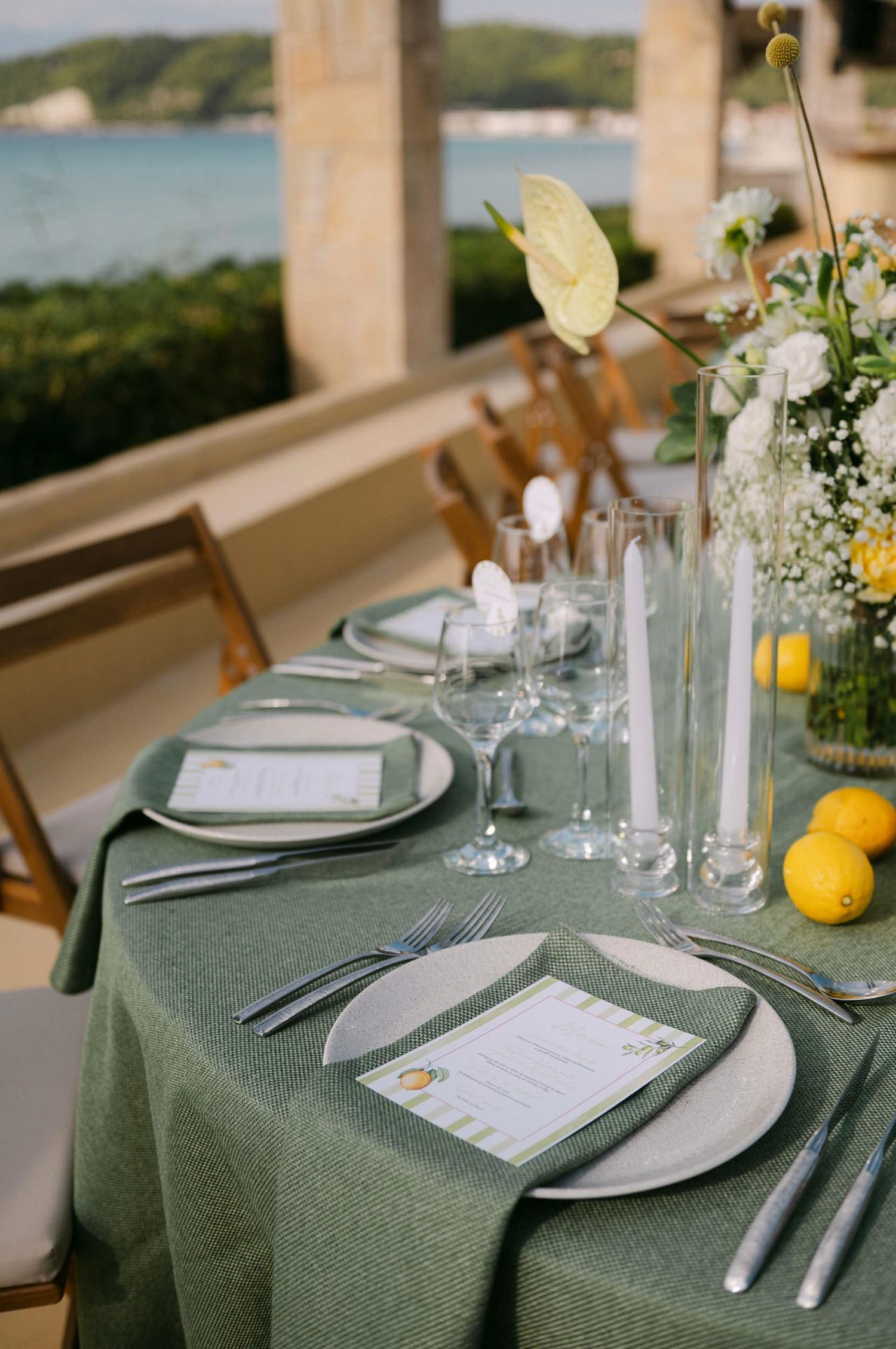 Elegant table settings with sage green tablecloths, white plates, and fresh citrus accents at a waterfront venue.
