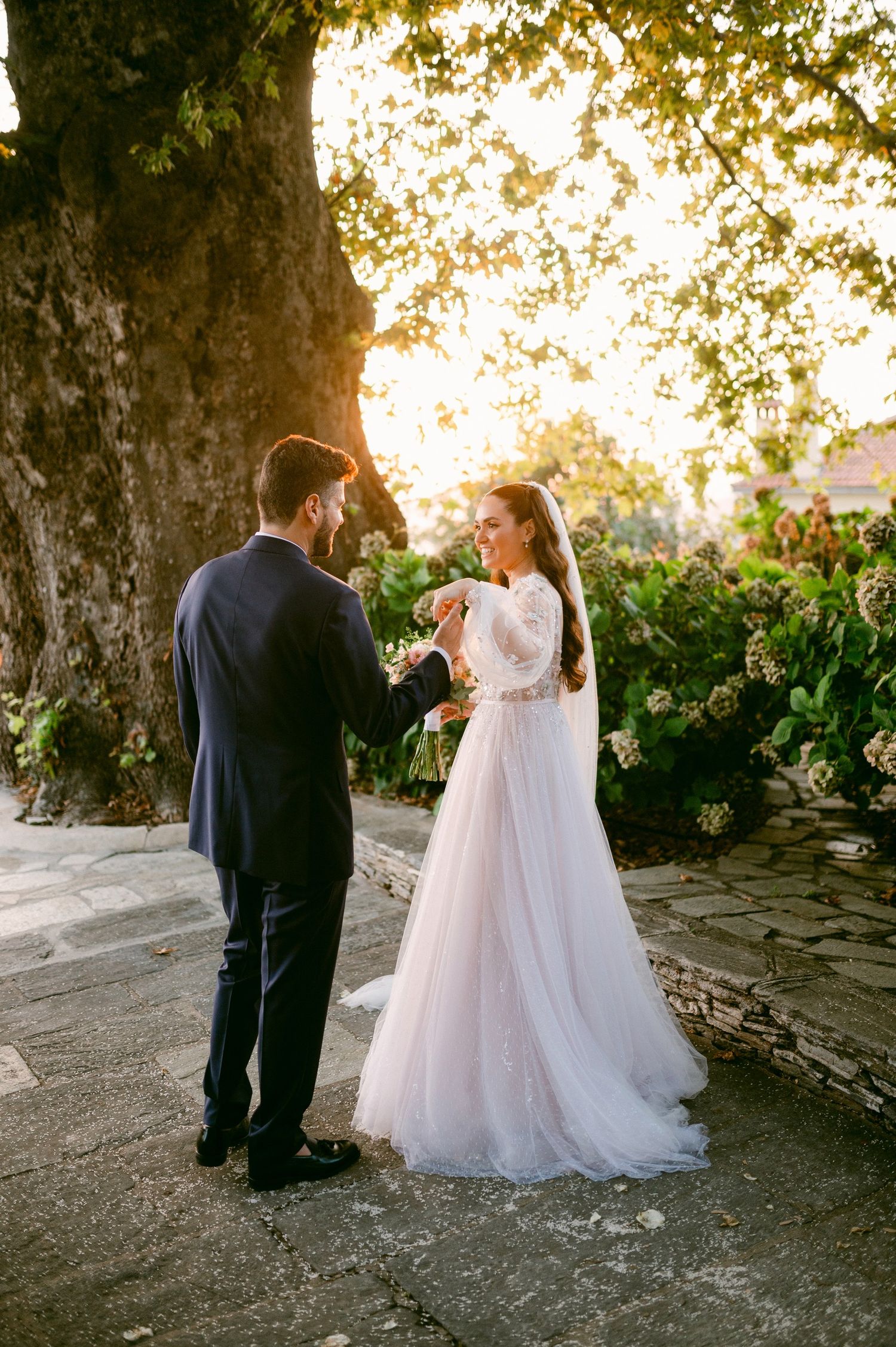 Elegant wedding couple shares an intimate moment at sunset under a tree during their outdoor ceremony.