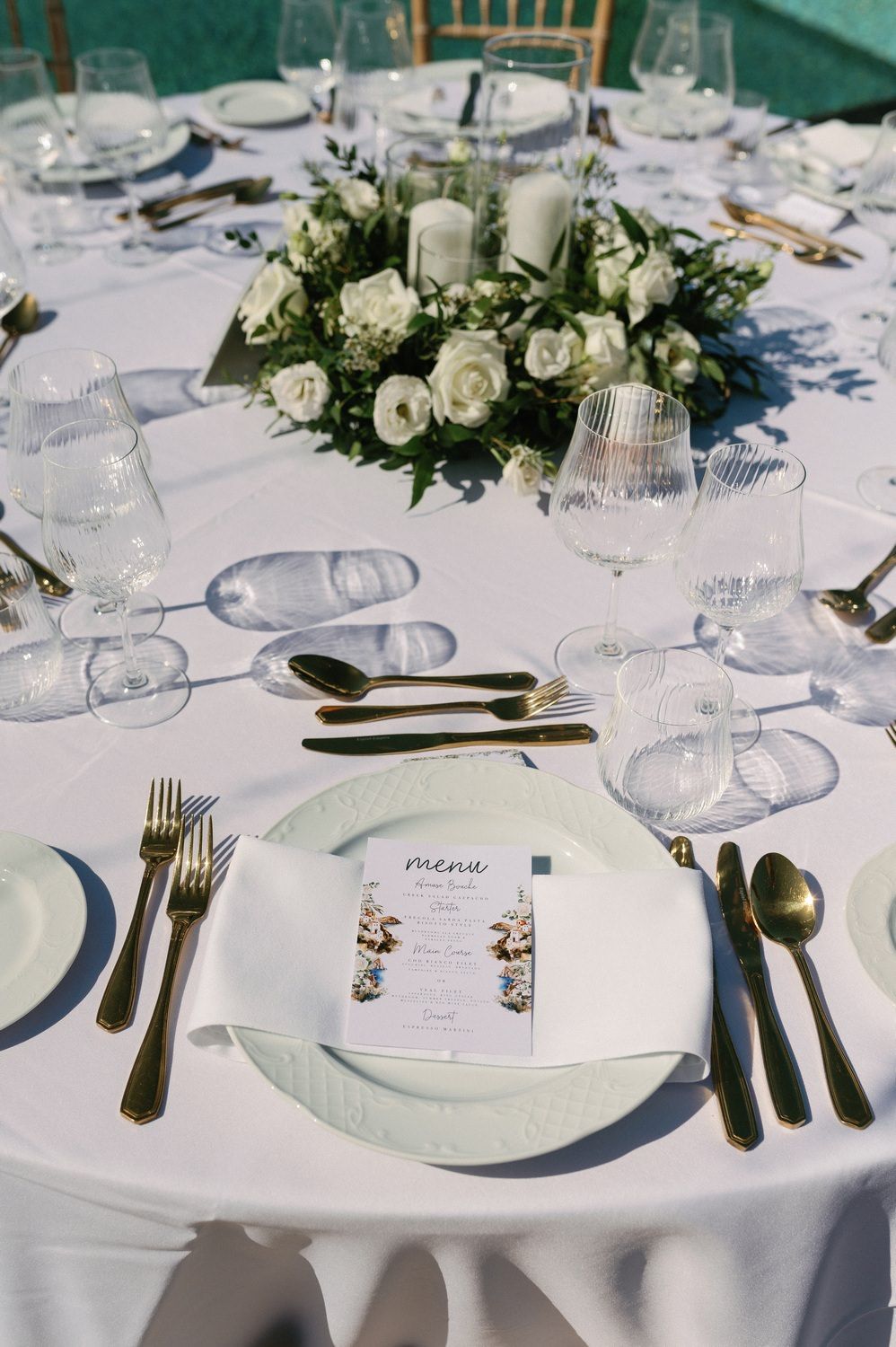 Elegant wedding table setting with white floral centerpiece, crystal glasses and formal place settings on round table.