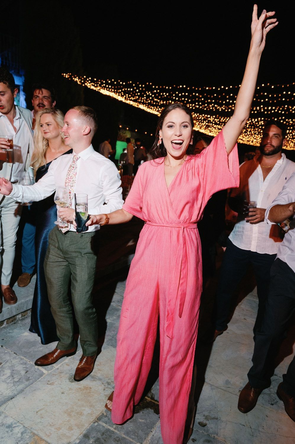 Party guests dancing joyfully under string lights at outdoor celebration.