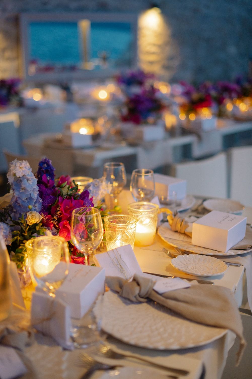 Elegant wedding reception table with glowing candles, purple flowers and formal place settings.