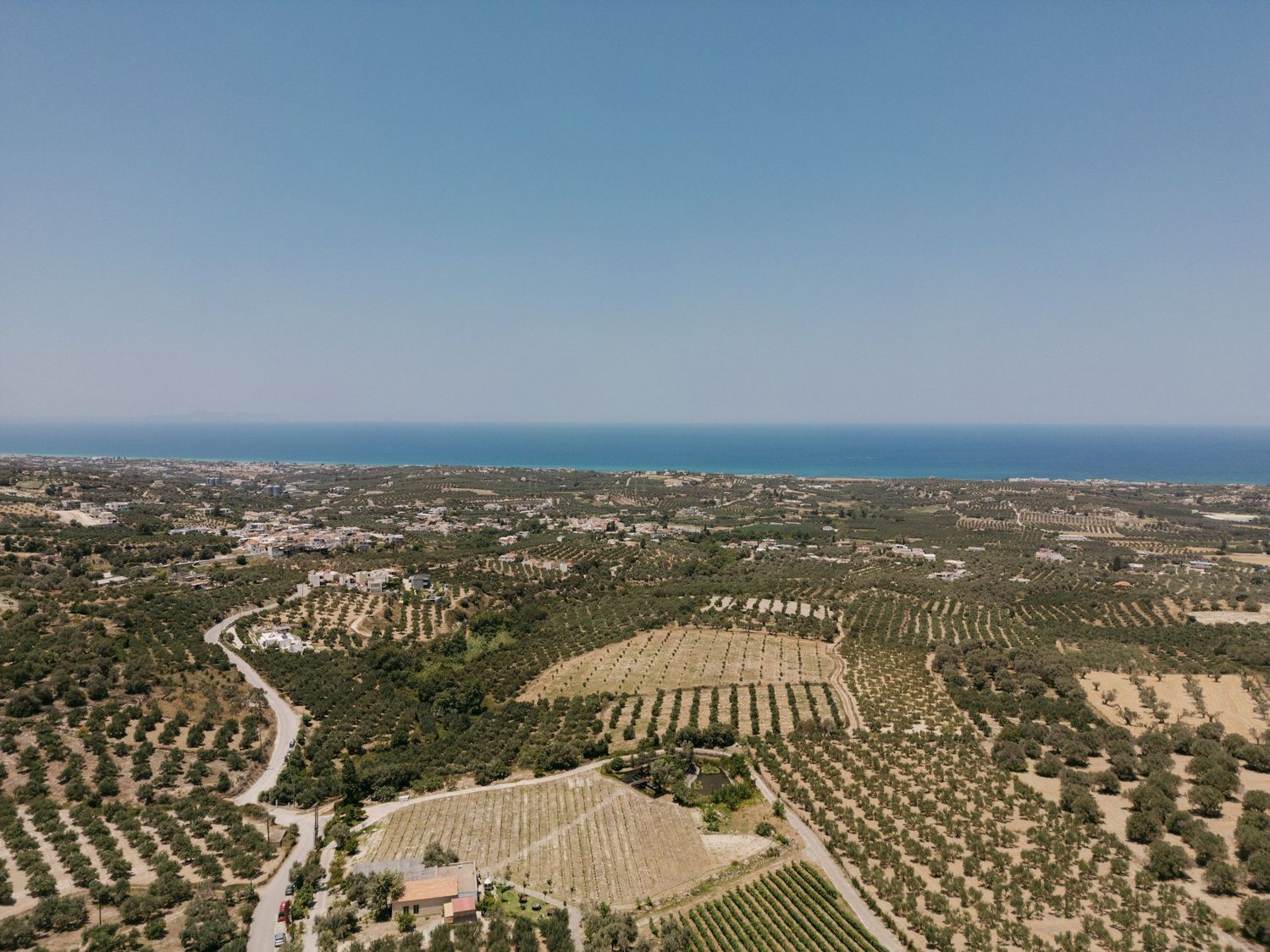 Aerial panoramic view of Agreco farms, olive groves and agricultural fields extending across Rethimno coastal landscape under blue sky.