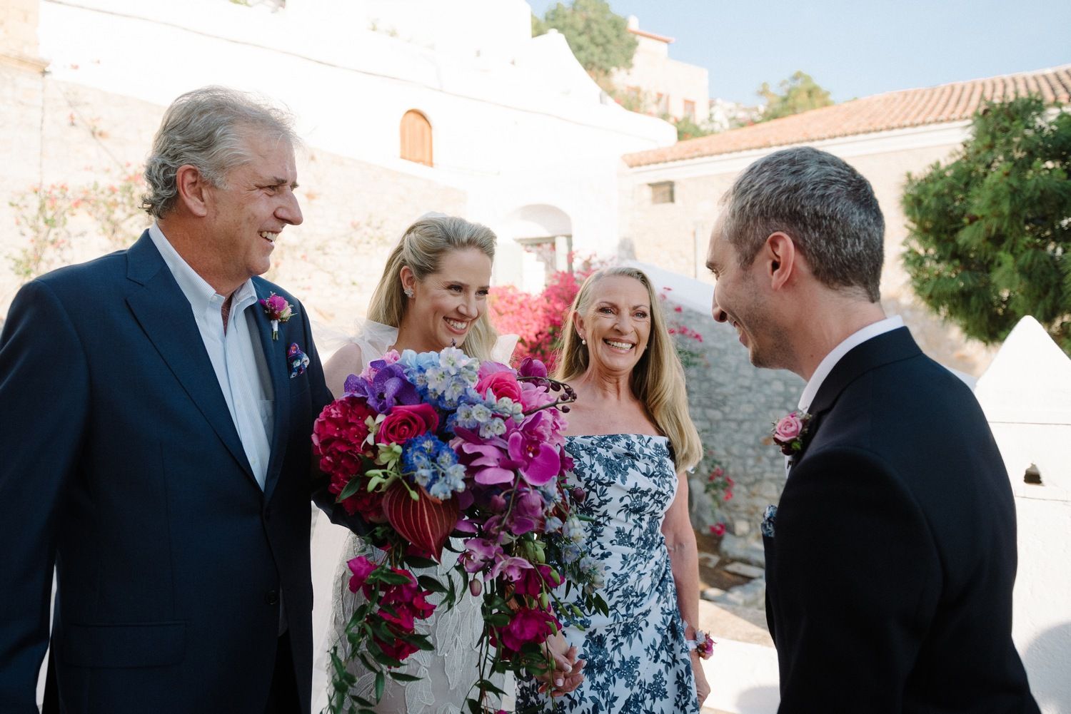 Wedding party conversation amid bright floral decorations at Mediterranean venue.