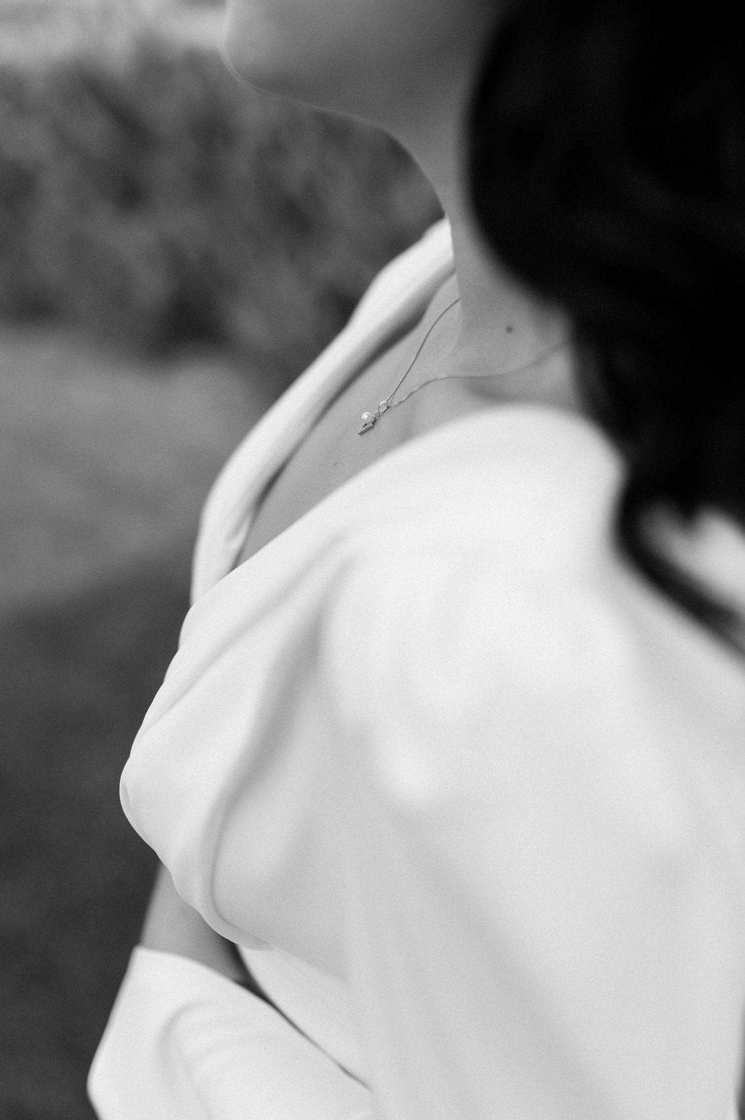 Artistic black and white detail shot of a white dress neckline with a dainty necklace visible.