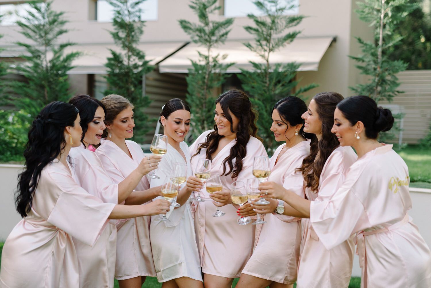 A group in matching silk robes toasts with champagne in an outdoor garden setting.