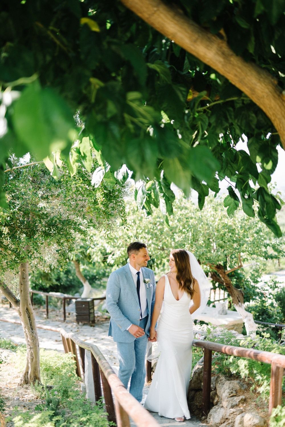 Newlyweds walking together under green tree canopy on garden path.