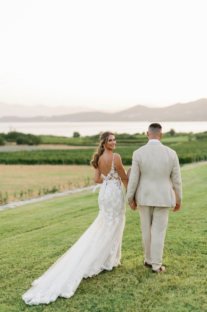 Wedding couple walking hand in hand on grassy hillside with mountain backdrop.