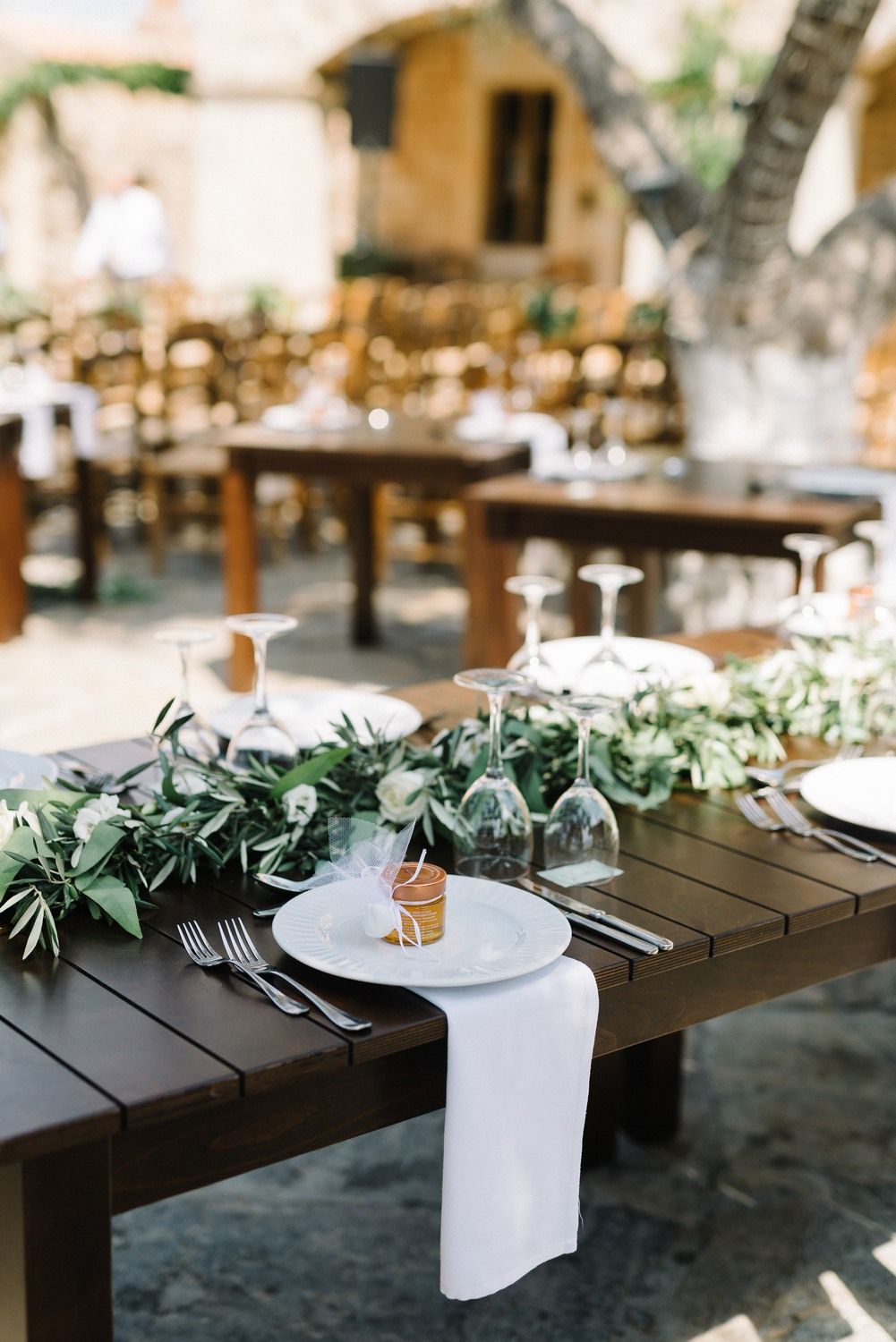 Elegant wedding table setting with greenery runners and white linens outdoors.