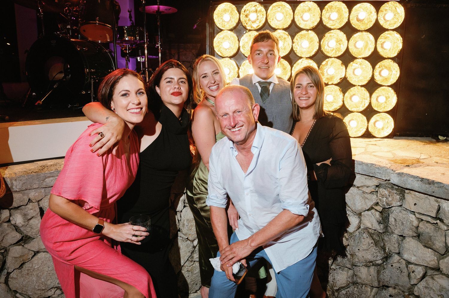Group photo at party with vintage-style lighting wall and stone backdrop.
