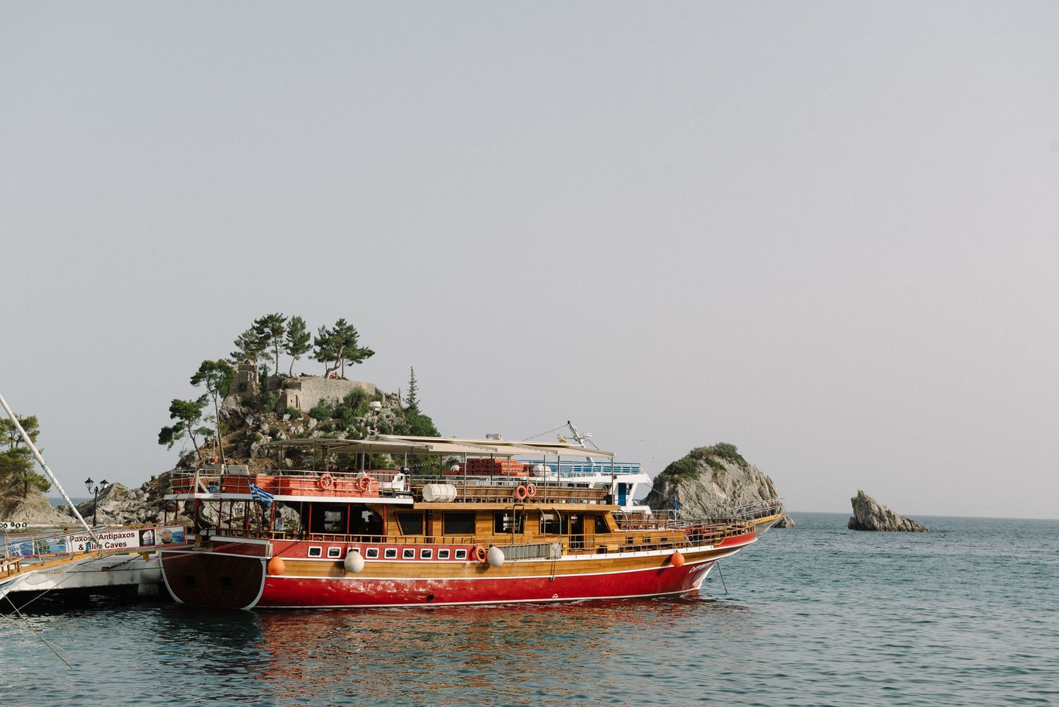 Traditional red wooden tour boat docked near rocky islands in clear blue waters.