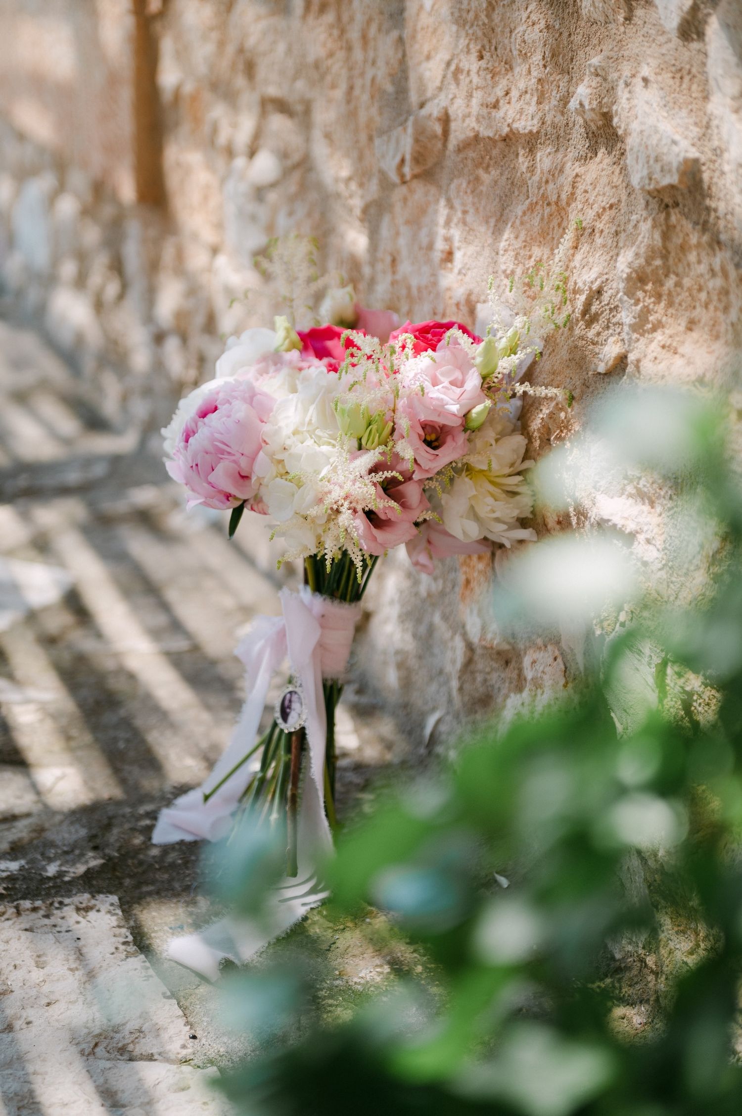 A delicate pink and white floral wedding bouquet rests against a textured stone wall with soft natural lighting.