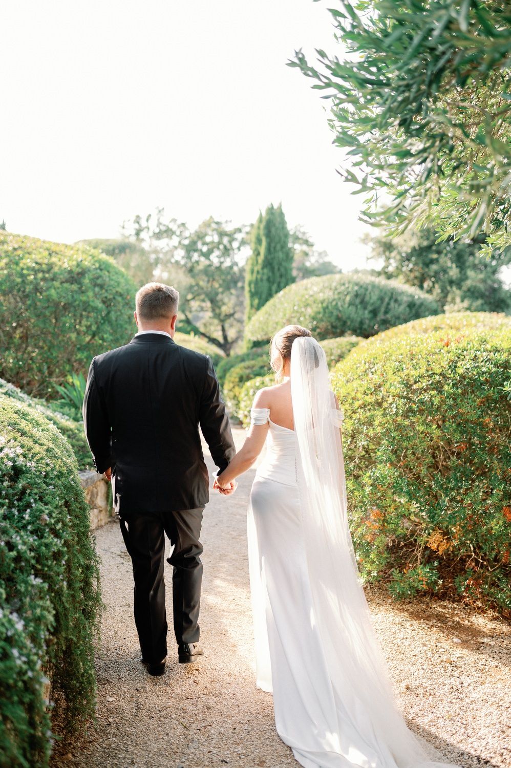 Newlyweds walking hand in hand down a romantic garden path.
