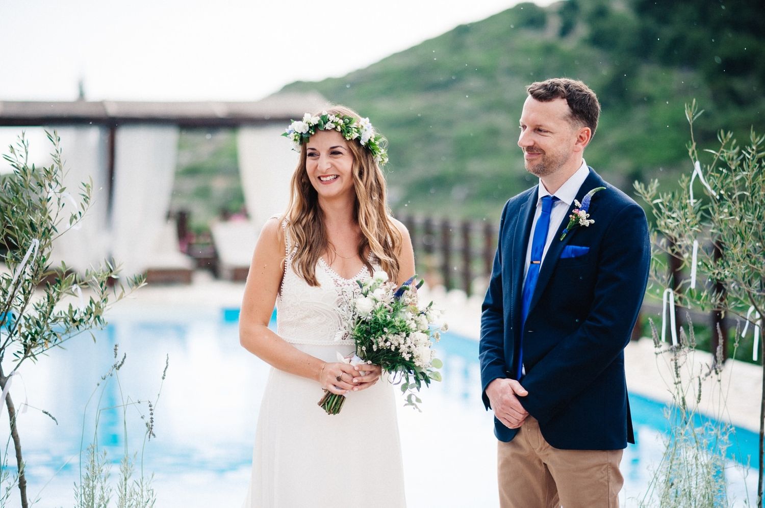 Elegant outdoor wedding ceremony beside pool with floral arrangements and mountain backdrop.