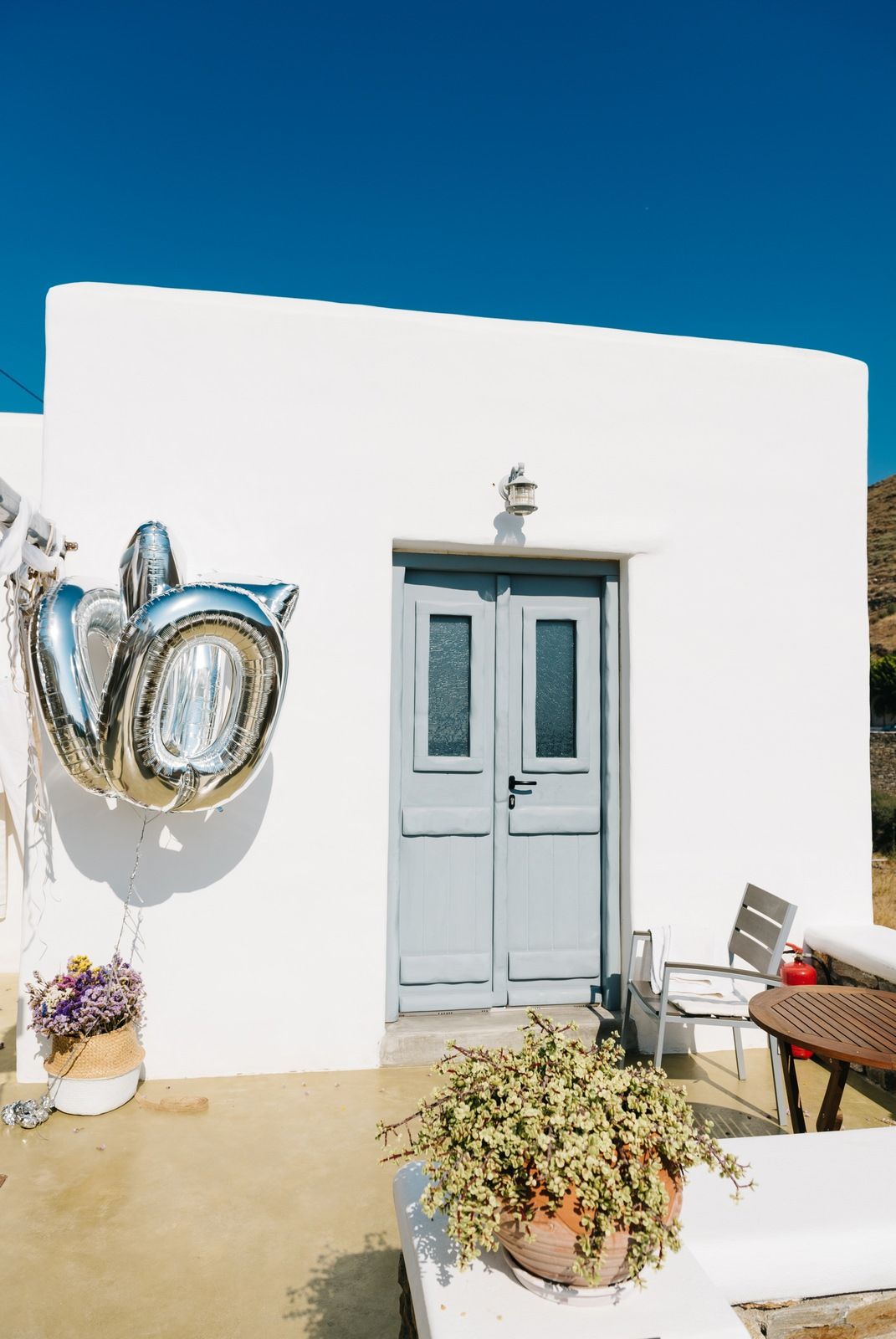 A light blue door and metallic decor adorns a white Mediterranean-style building under bright blue skies.