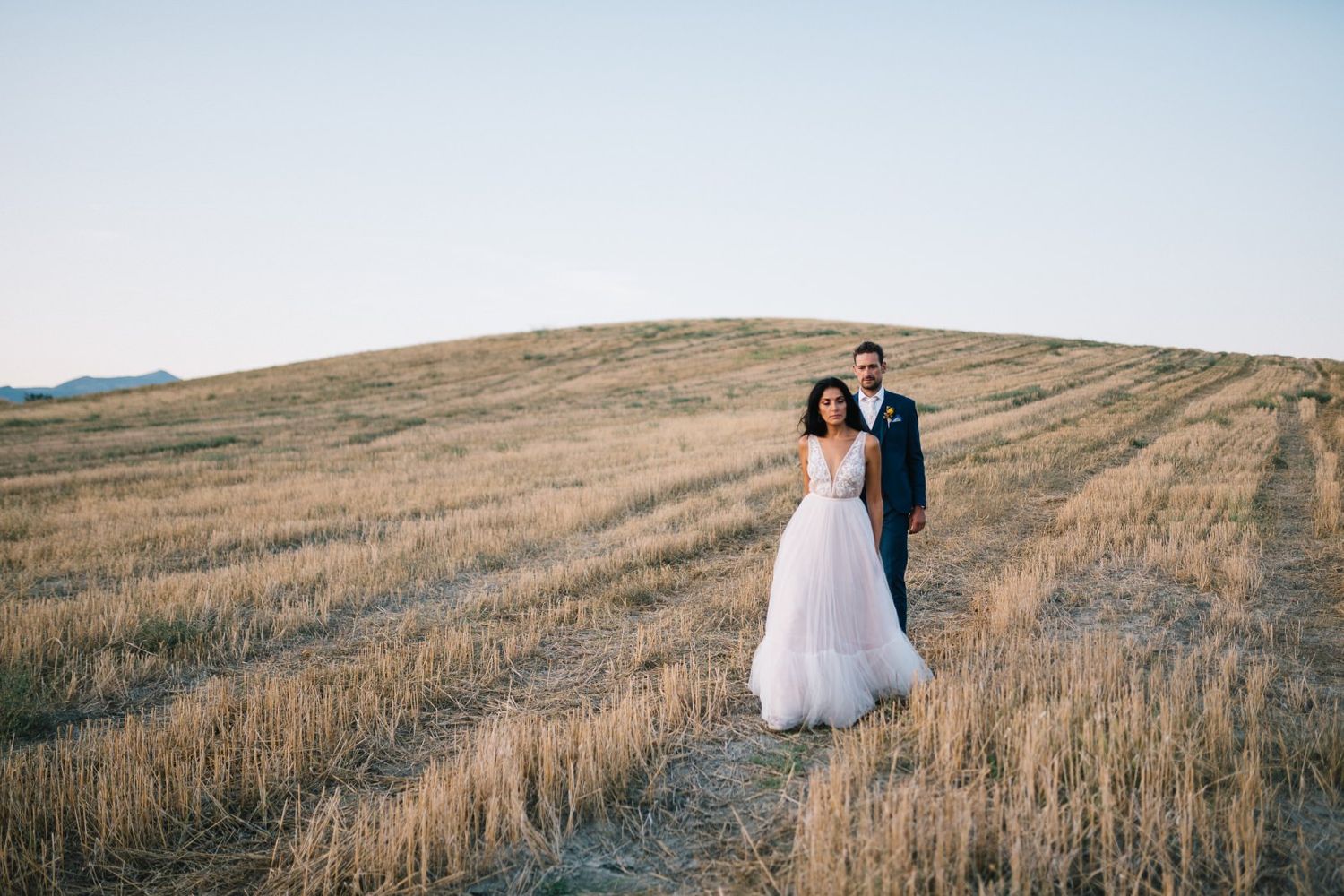 A couple shares an intimate moment on a golden hillside path at sunset.