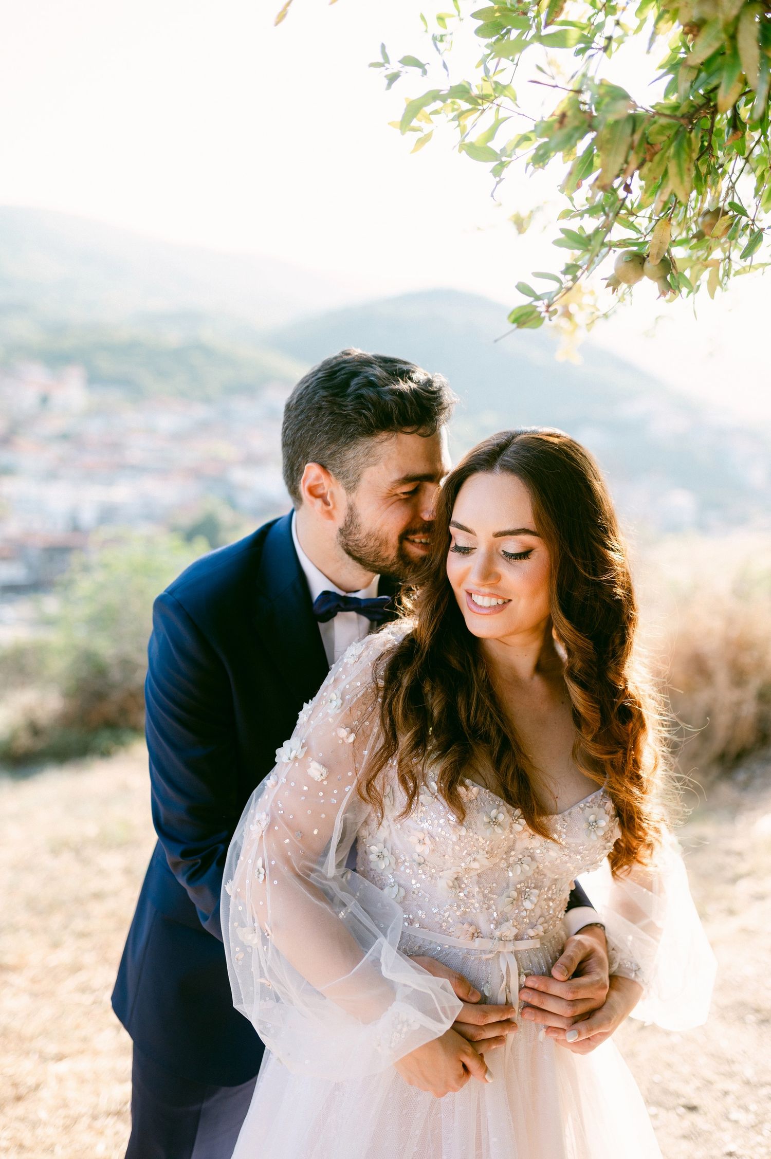 Elegant couple embracing on hilltop during sunset wedding photoshoot with mountains in background.