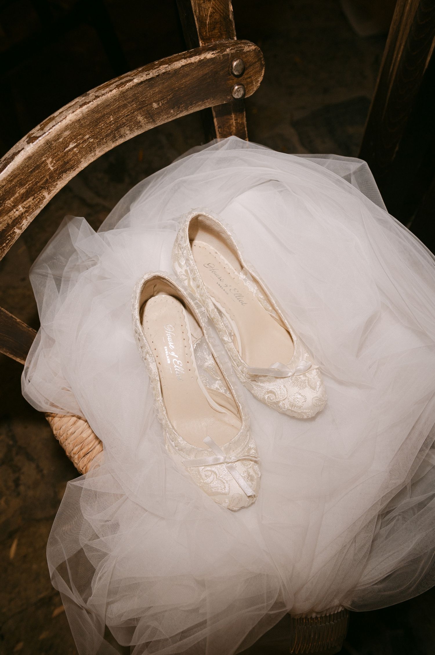 White tulle wedding dress and cream-colored bridal shoes arranged artistically against dark wood background.