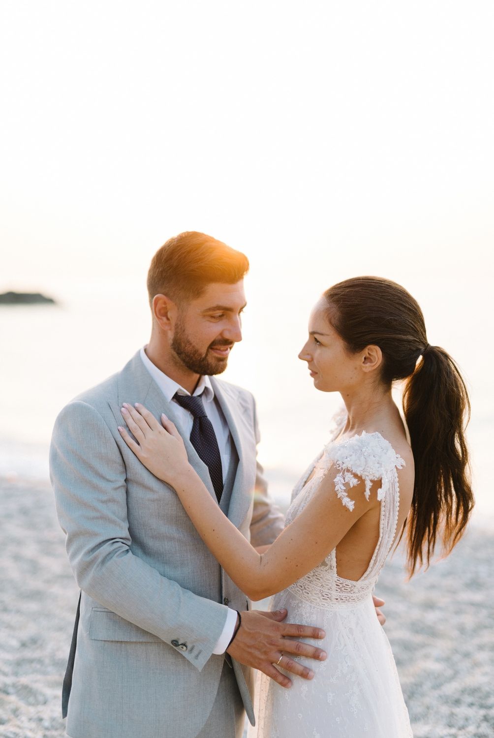 An intimate beachside wedding portrait shows a couple in elegant attire sharing a romantic moment.