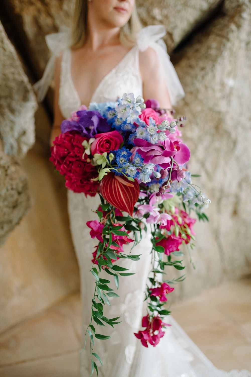 Vibrant cascading bridal bouquet with pink and purple flowers against white wedding dress.