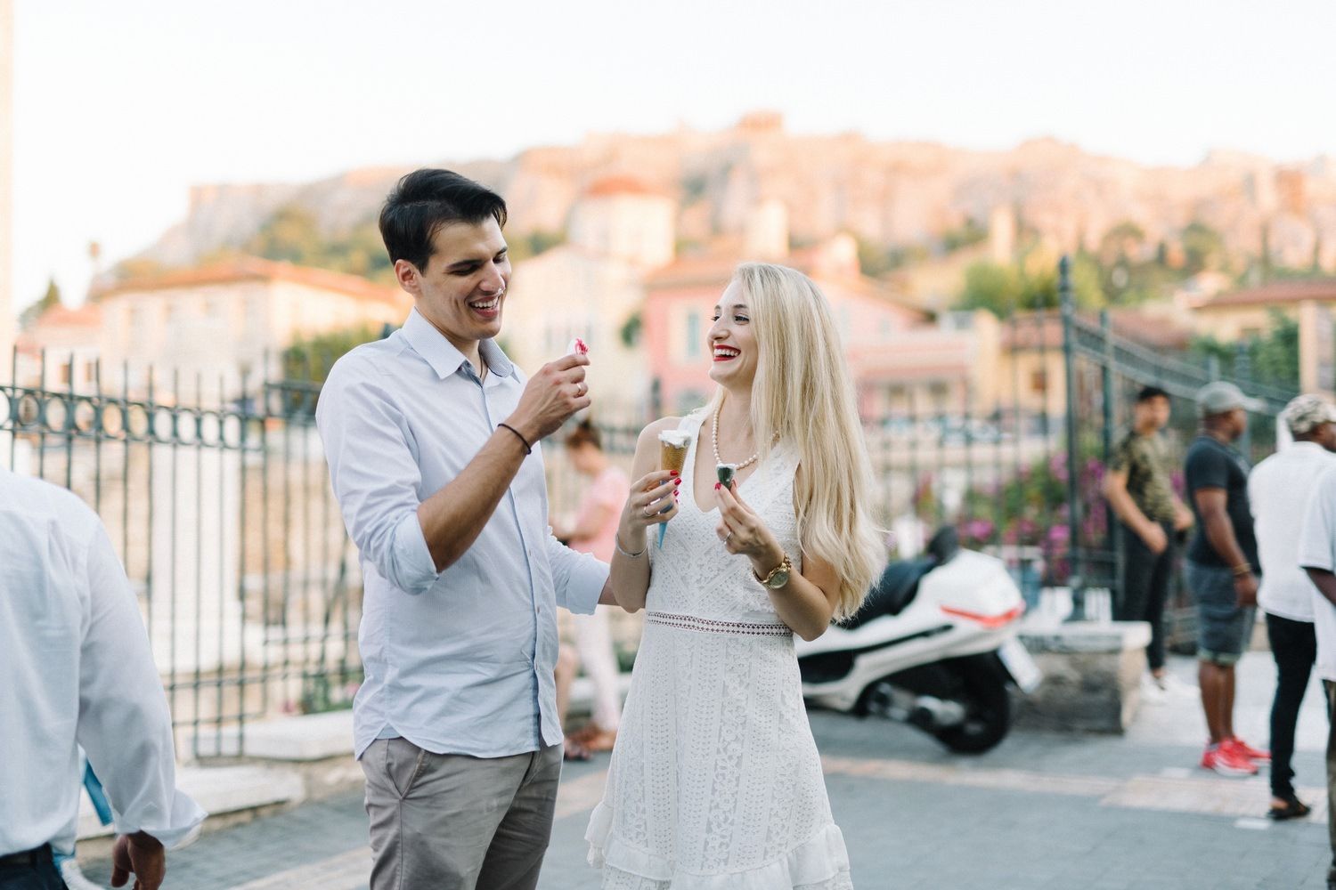 Couple enjoying gelato together with the Acropolis visible in the background during sunset.